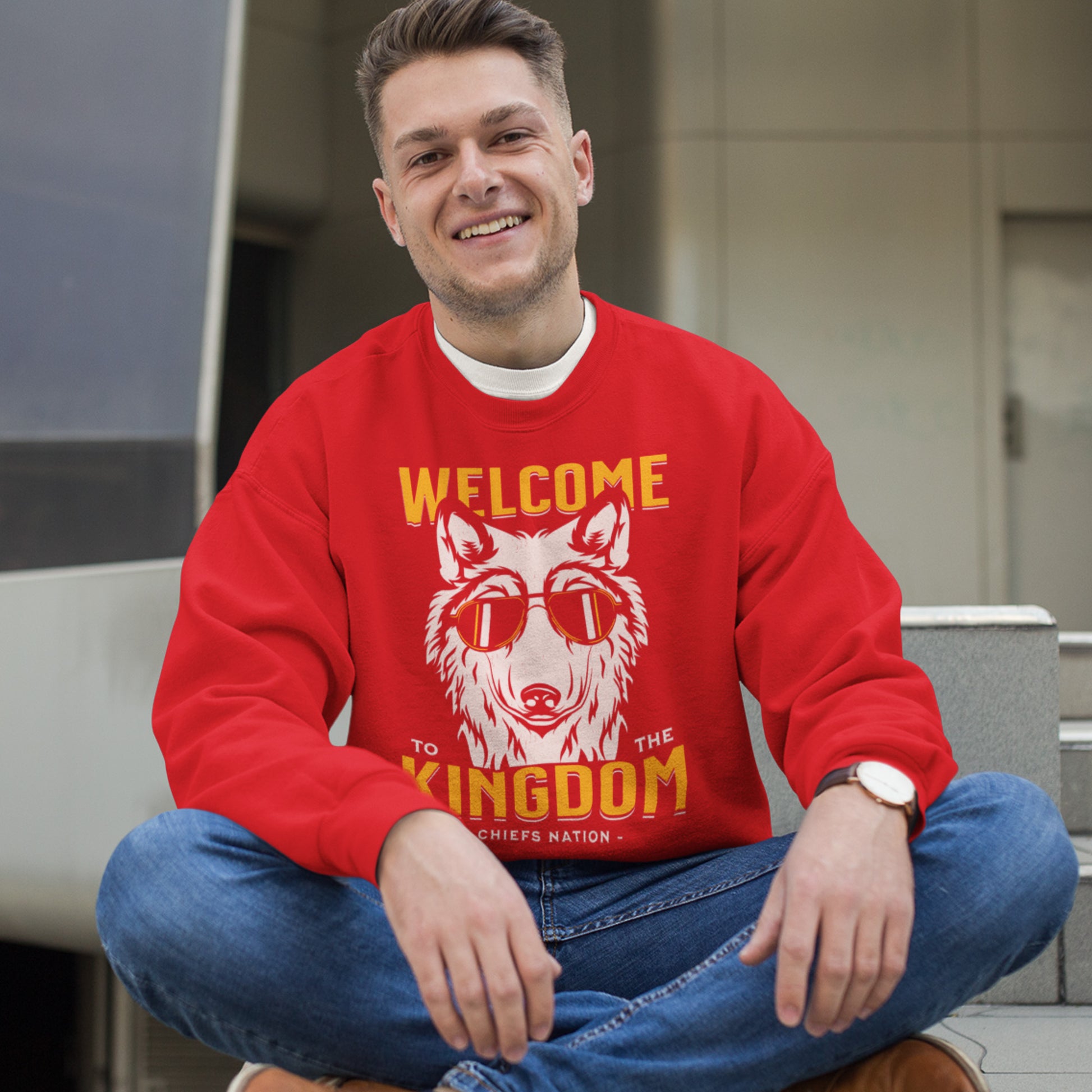 KC Swag Kansas City Chiefs Distressed White & Gold Cool Wolf Kingdom on a Red Crewneck Sweatshirt worn by a male model seating in front of a downtown building