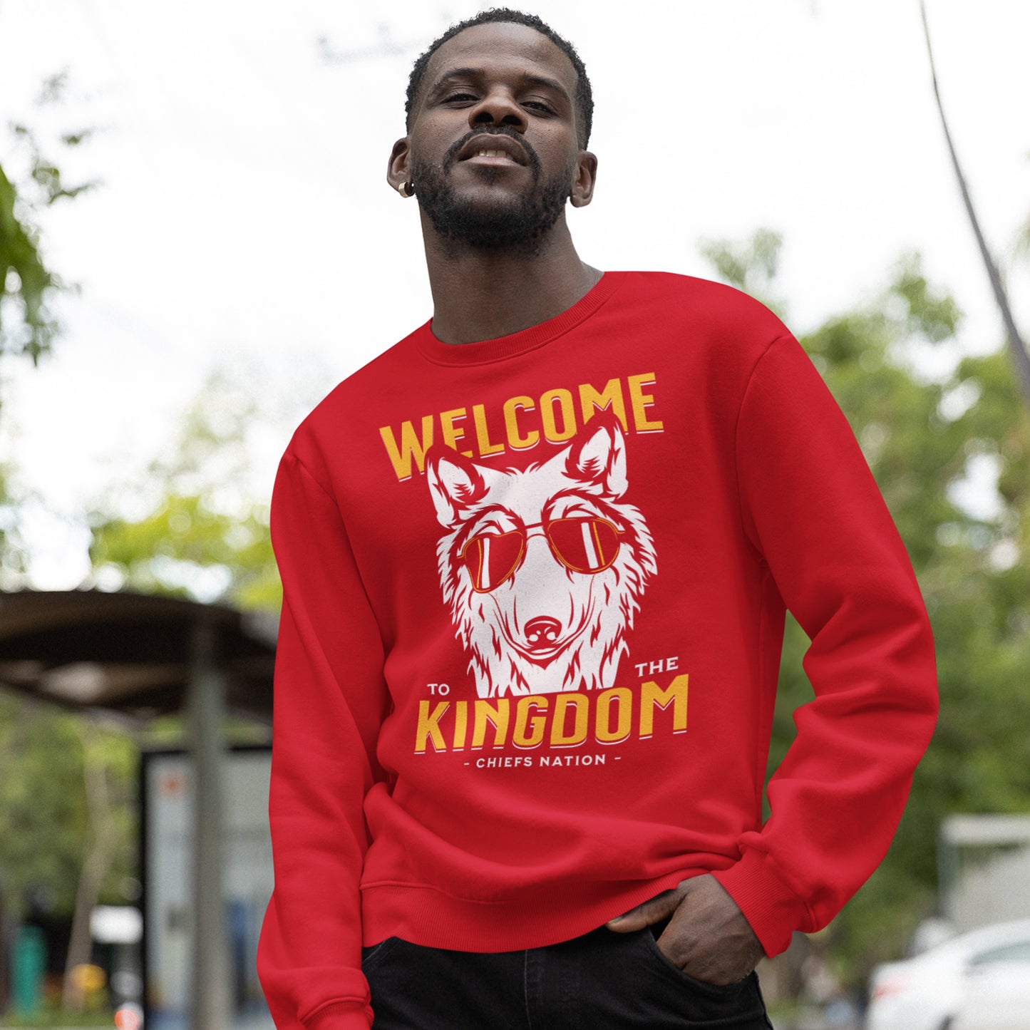 KC Swag Kansas City Chiefs Distressed White & Gold Cool Wolf Kingdom on a Red Crewneck Sweatshirt worn by a male model with his hand in his jeans' pocket while standing in a public park