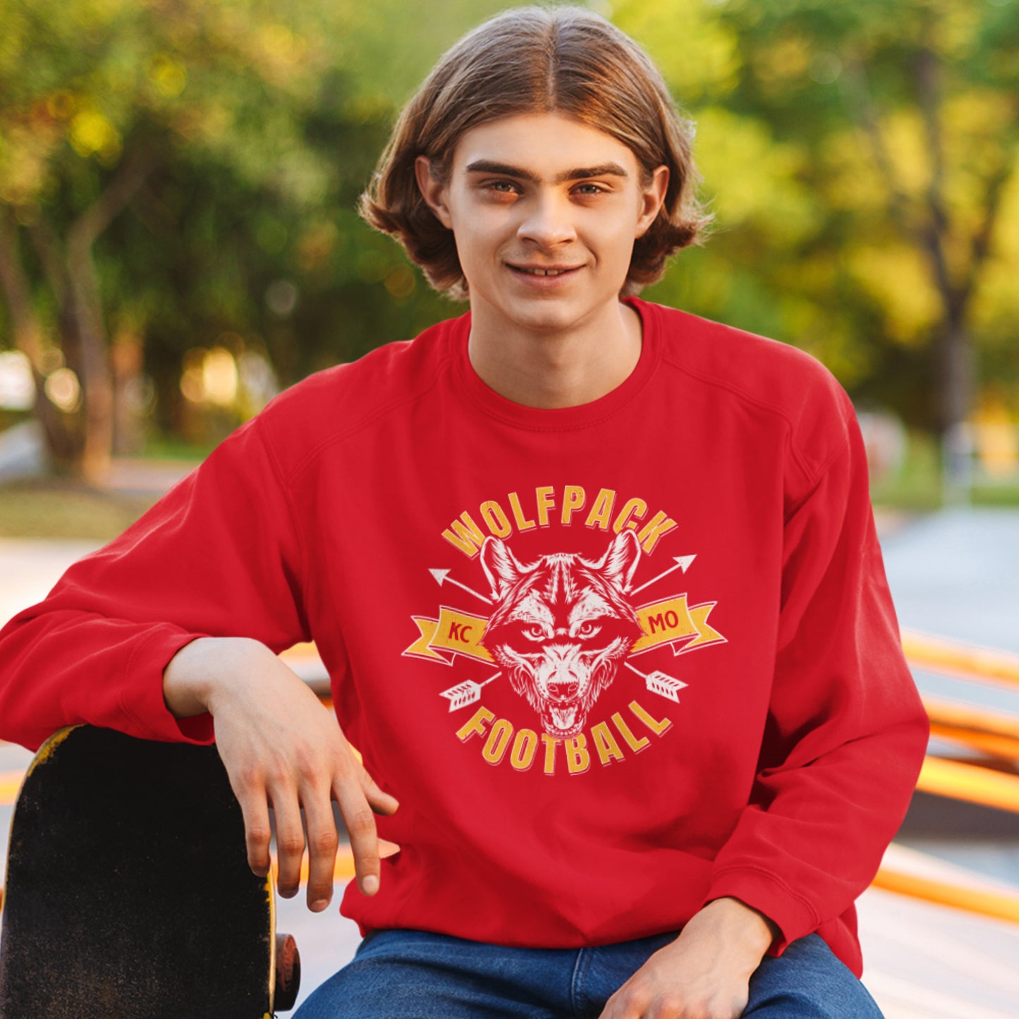 KC Swag Kansas City Chiefs Distressed White & Gold Wolfpack Football on a Red Crewneck Sweatshirt worn by a male model with his skateboard sitting in a public skatepark