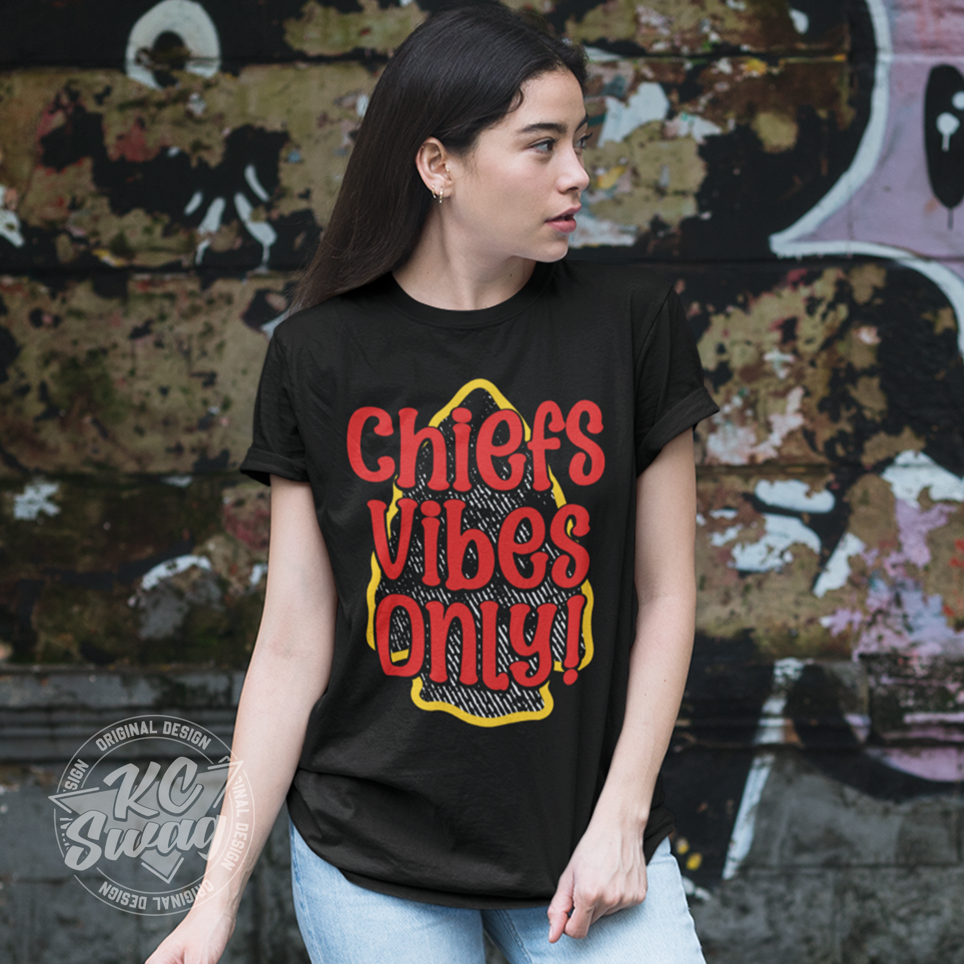 KC Swag - Kansas City Chiefs CHIEFS VIBES ONLY! on black unisex t-shirt worn by male model walking on sidewalk next to brick wall worn by female model standing in front of graffitied wall in urban alley