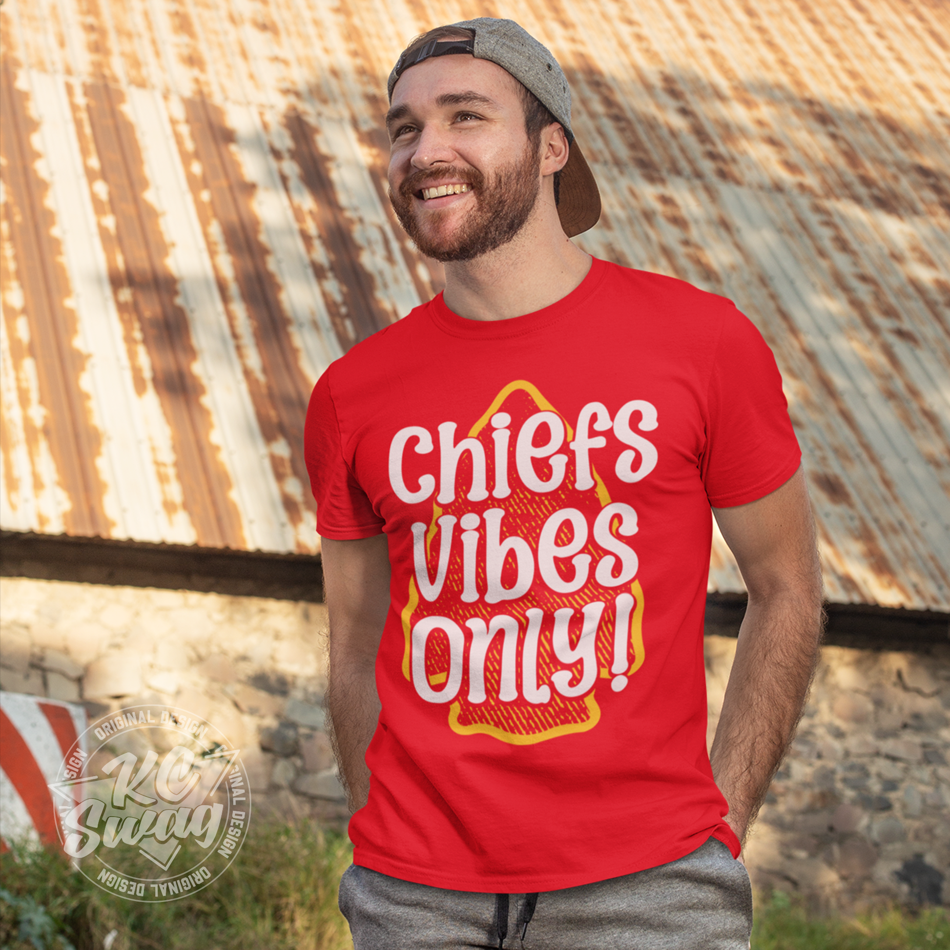 KC Swag - Kansas City Chiefs CHIEFS VIBES ONLY! on red unisex t-shirt worn by male model standing in front of ald rusty metal barn