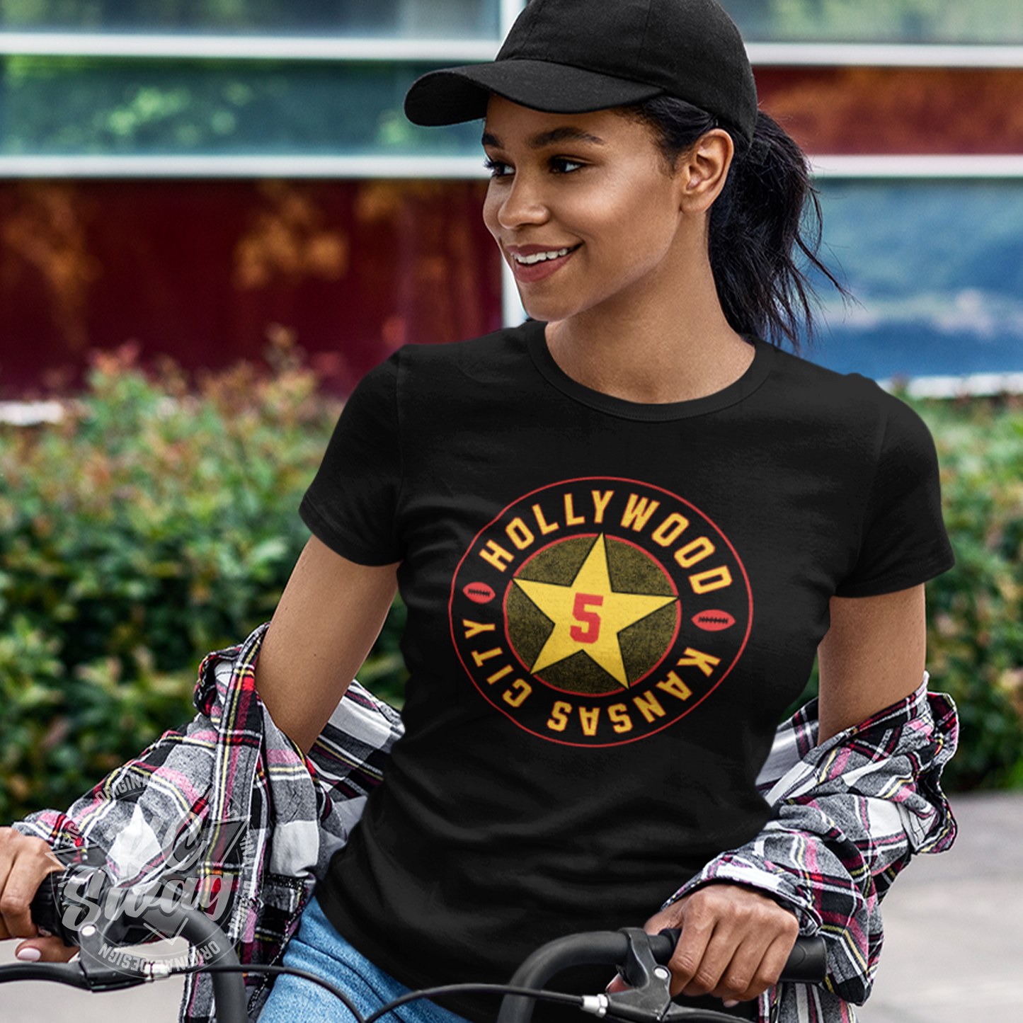 KC Swag - Kansas City Chiefs HOLLYWOOD BROWN STAR on black unisex t-shirt worn by female model on bake outside colorful building and bushes
