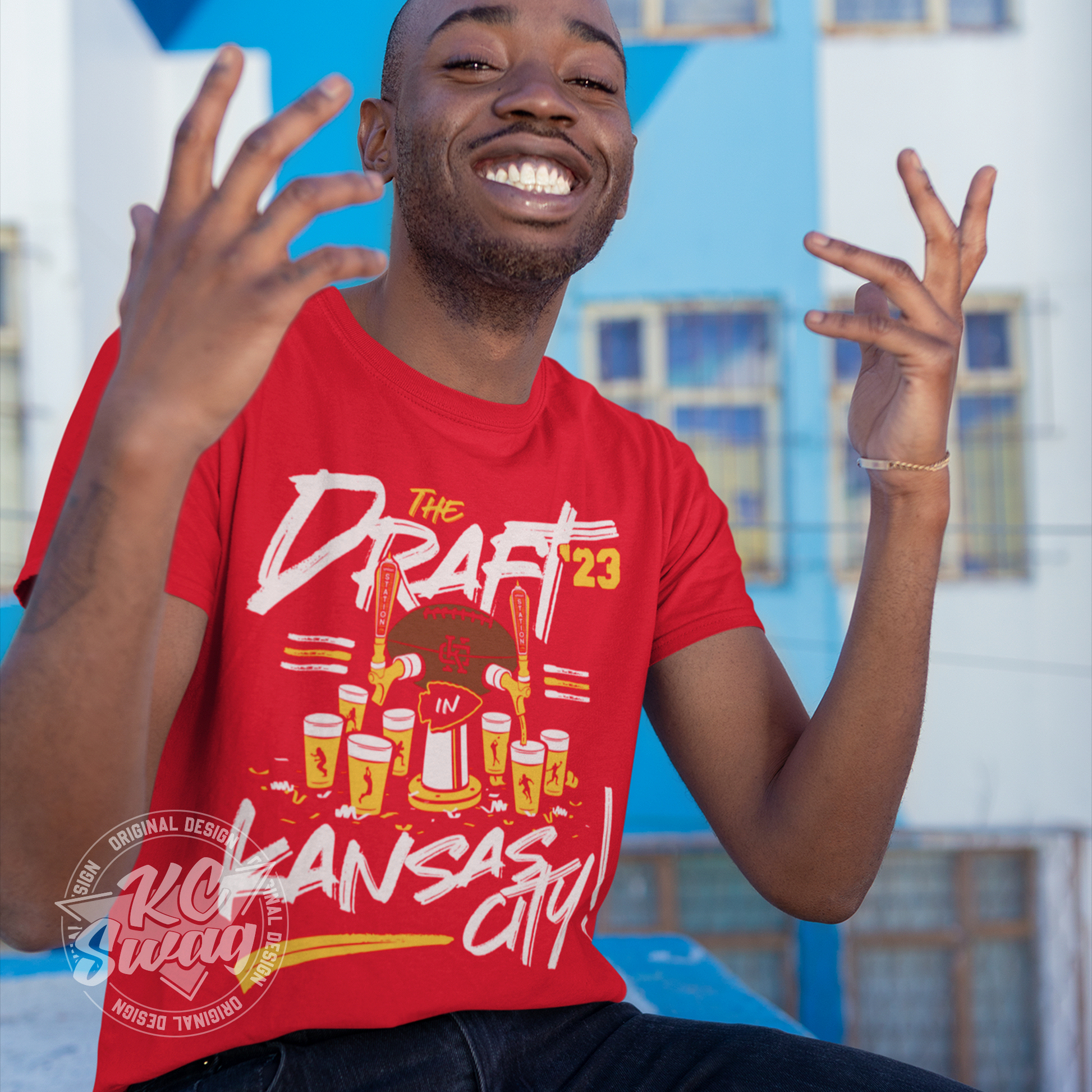 KC Swag - Kansas City Chiefs 2023 NFL DRAFT IN KC UNION STATION on red unisex t-shirt worn by male model sitting in front of a blue building
