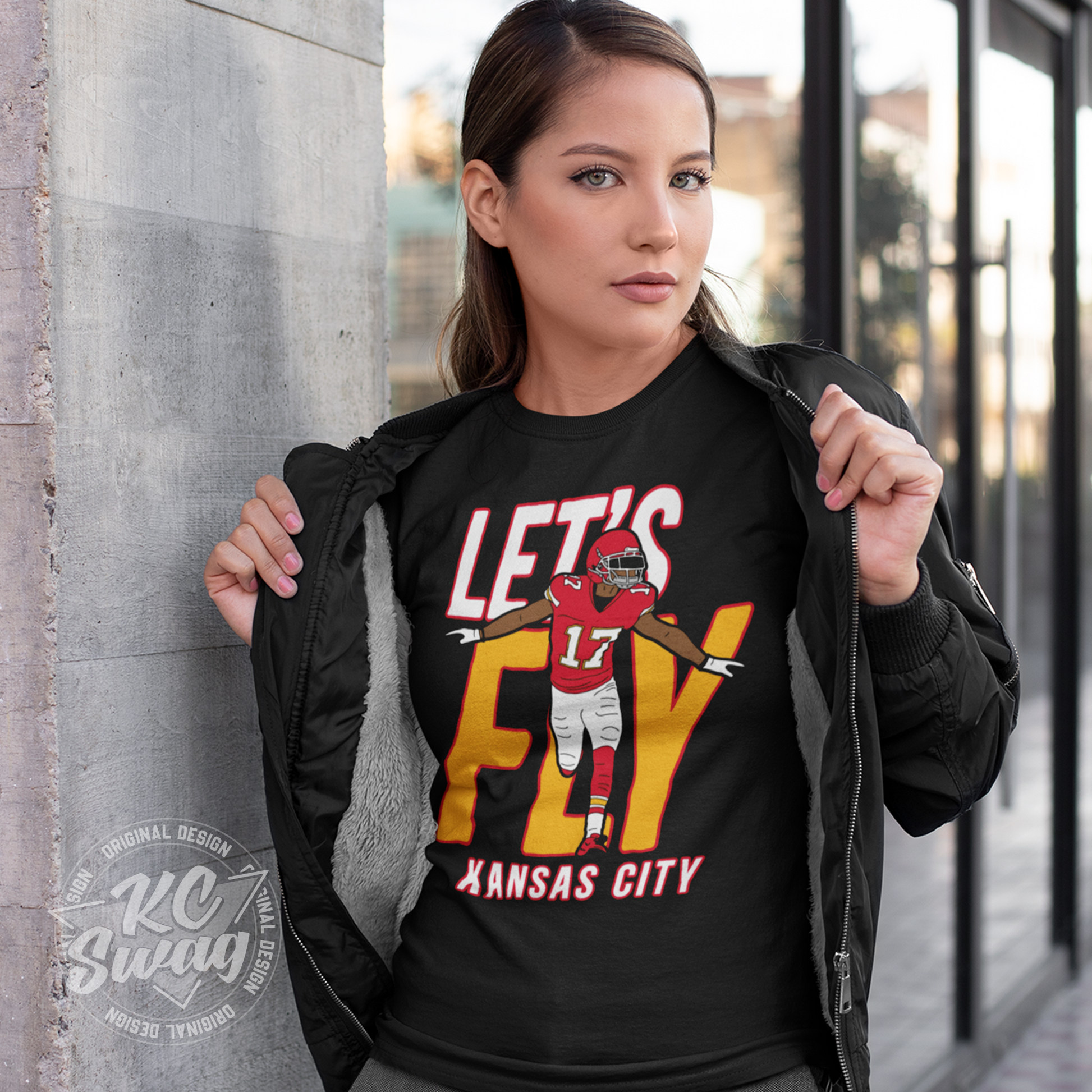 KC Swag - Kansas City Chiefs LET'S FLY HARDMAN KANSAS CITY on black unisex t-shirt worn by female model under an open jacket leaning on a concrete pillar