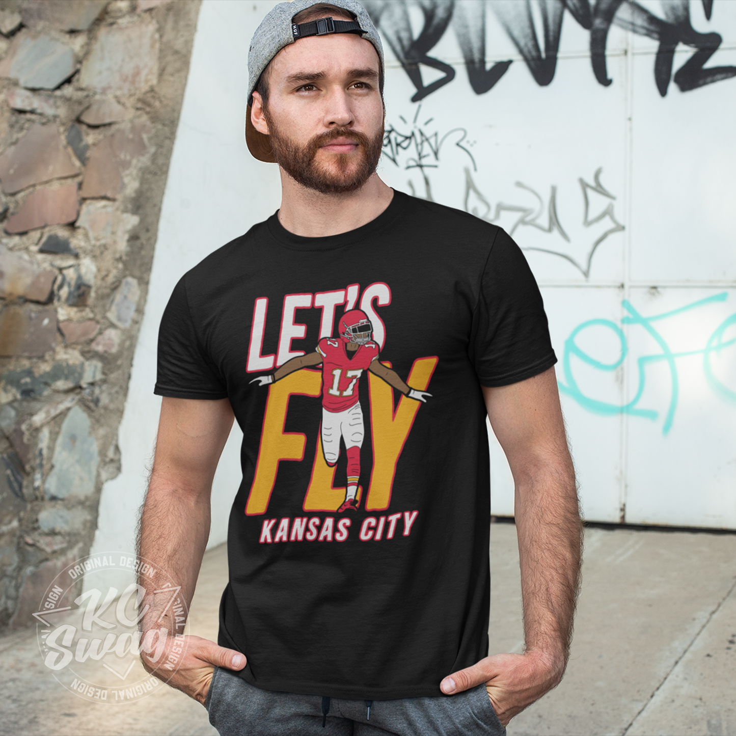 KC Swag - Kansas City Chiefs LET'S FLY HARDMAN KANSAS CITY on black unisex t-shirt worn by male model standing in front of a graffitied wall in a public park