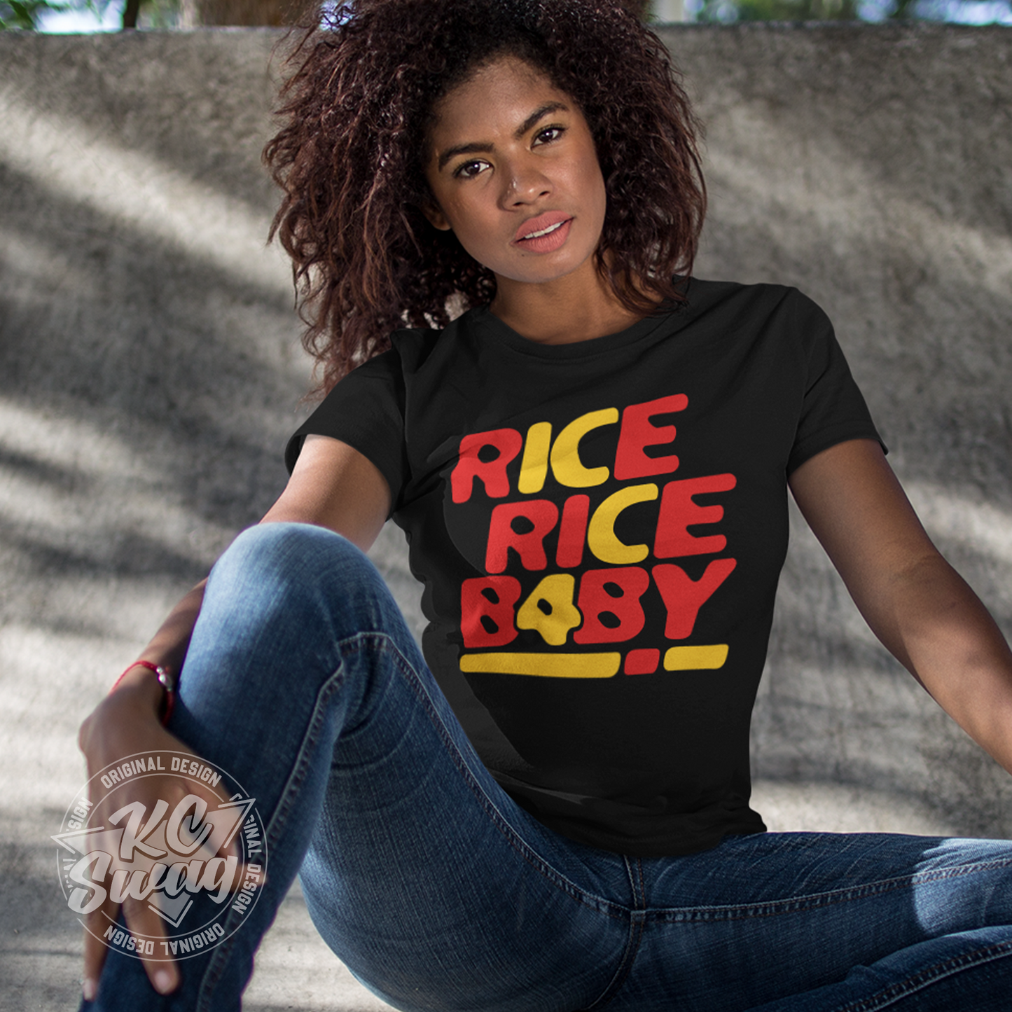 KC Swag - Kansas City Chiefs RICE RICE BABY KC 4 on black unisex t-shirt worn by female model sitting in front of a concrete wall in a public park