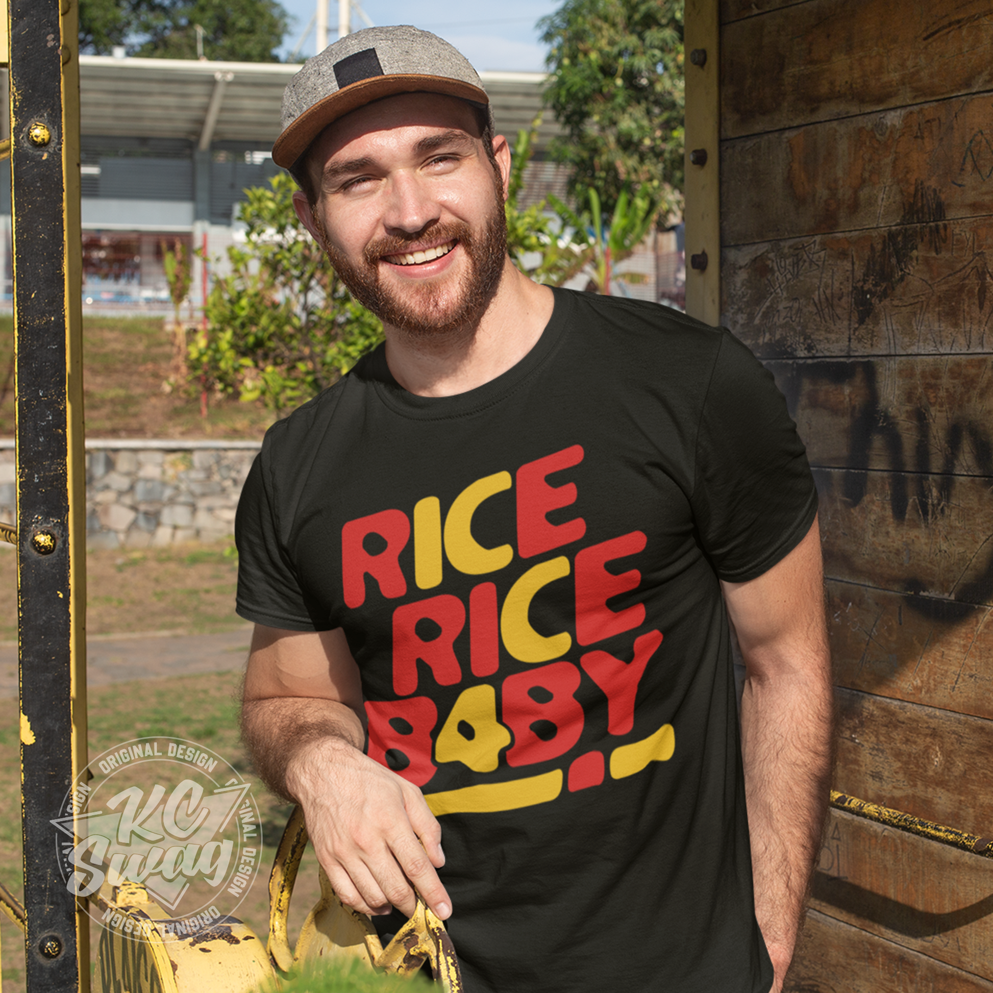 KC Swag - Kansas City Chiefs RICE RICE BABY KC 4 on black unisex t-shirt worn by male model leaning on rusty garden hose reel on farm