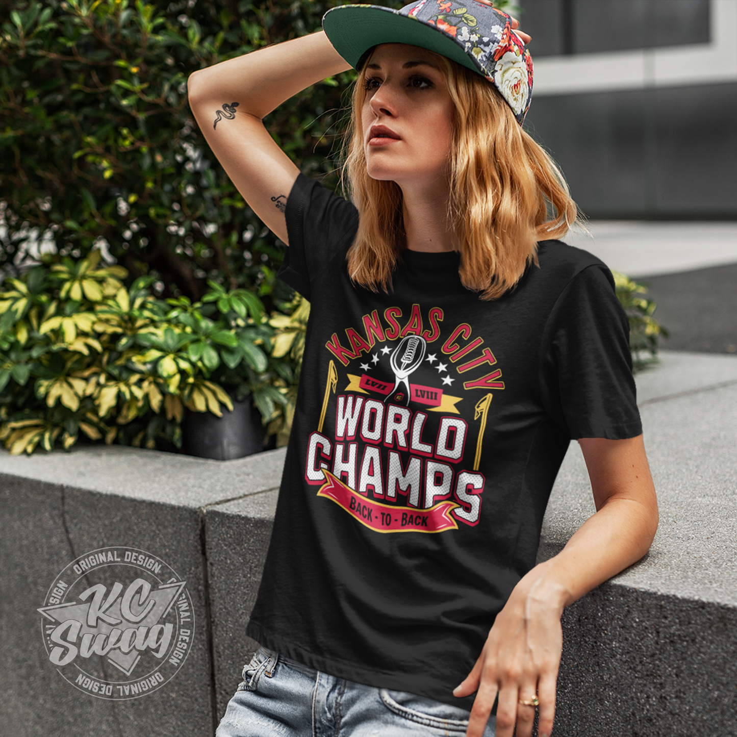 KC Swag - Kansas City Chiefs KANSAS CITY WORLD CHAMPS BACK TO BACL LVII LVIIIon black unisex t-shirt worn by female model leaning on concrete wall in outdoor plaza