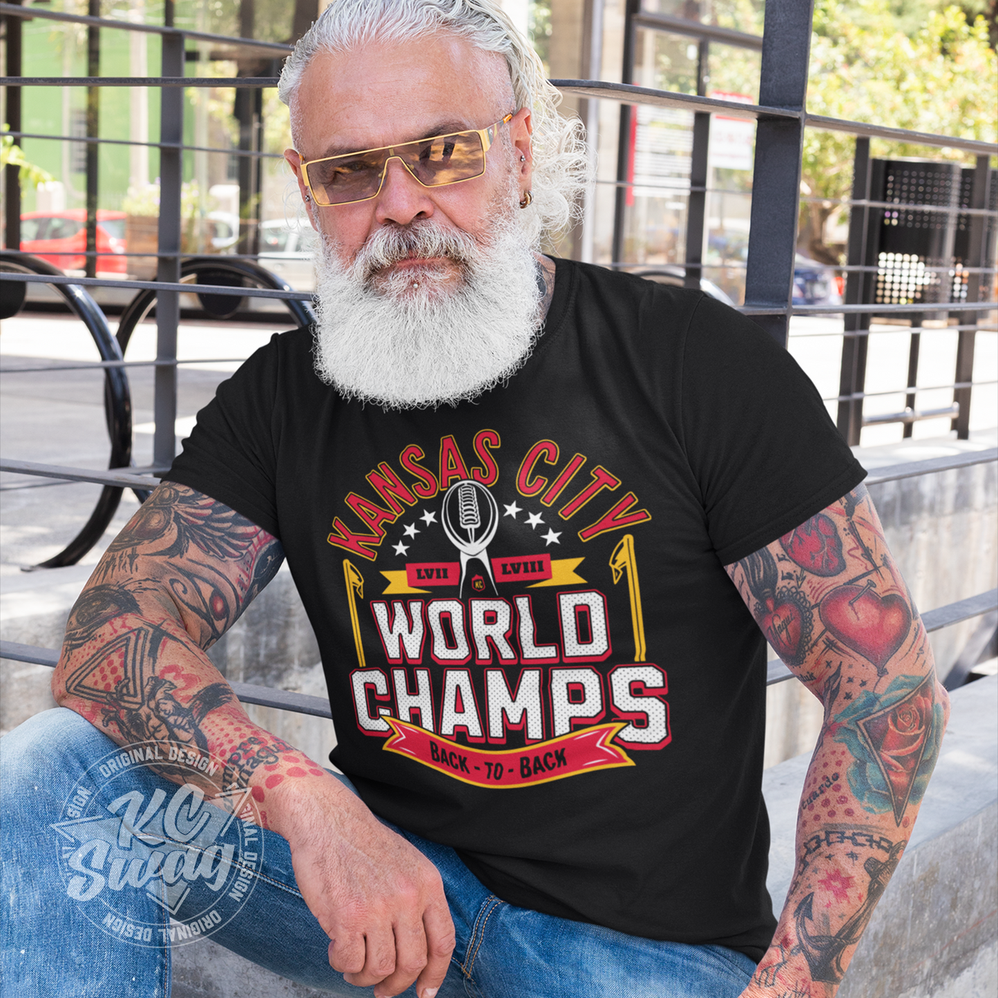 KC Swag - Kansas City Chiefs KANSAS CITY WORLD CHAMPS BACK TO BACL LVII LVIIIon black unisex t-shirt worn by bearded male model sitting on outdoor restaurant patio