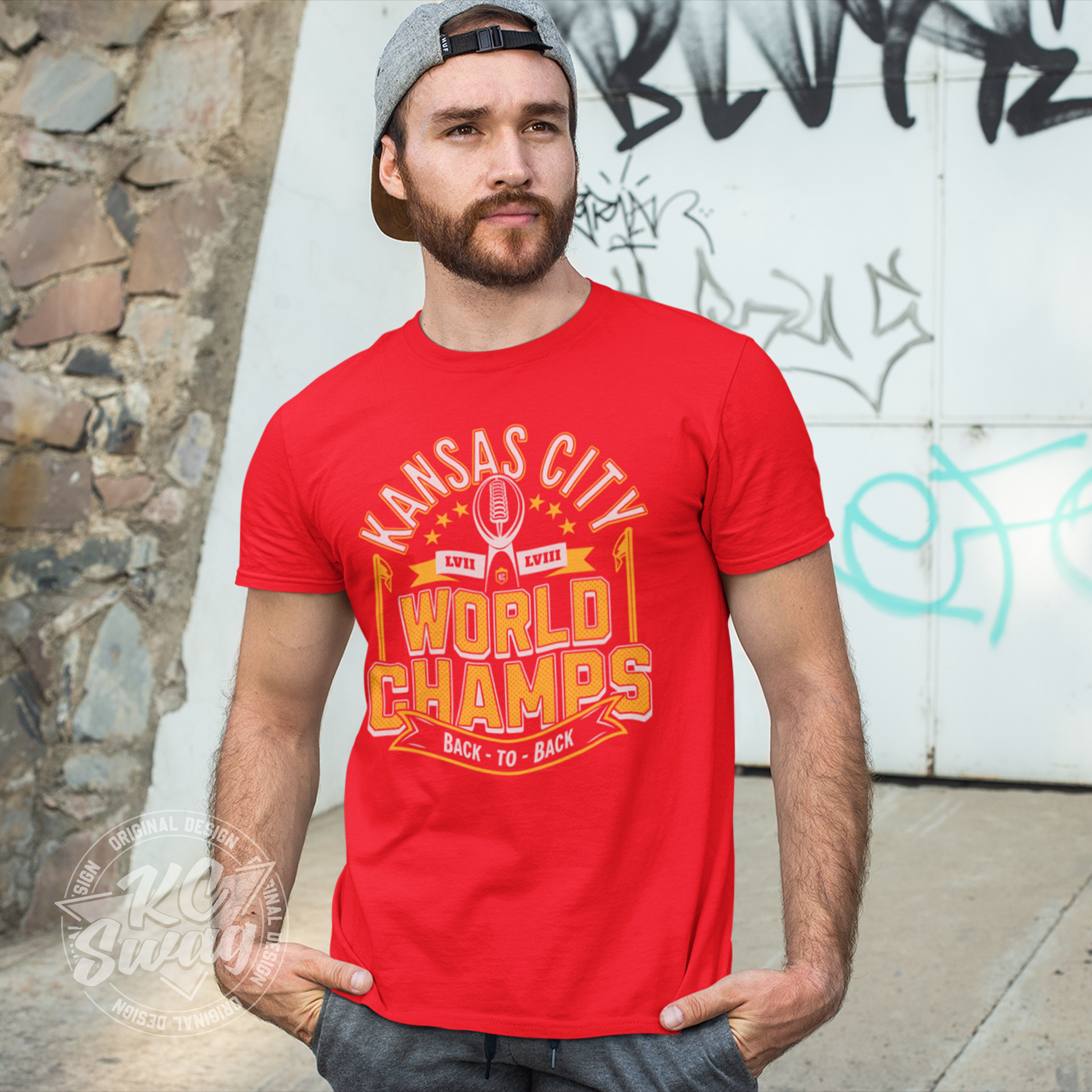 KC Swag - Kansas City Chiefs KANSAS CITY WORLD CHAMPS BACK TO BACL LVII LVIIIon red unisex t-shirt worn by male model standing in front of graffitied wall in public park