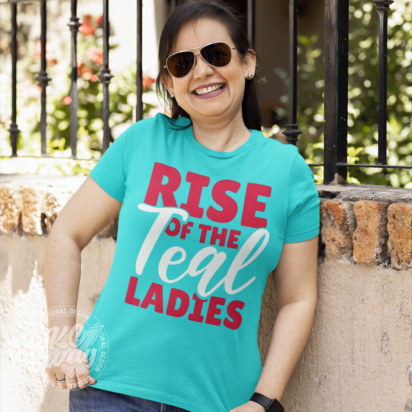 KC Swag - Kansas City Current, Rise Of The Teal Ladies design on a teal unisex t-shirt worn by female model leaning on a cement wall in aviator sunglasses