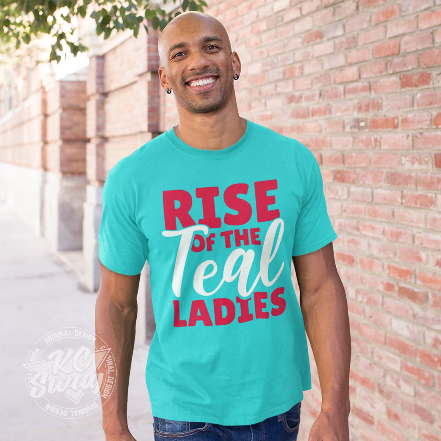 KC Swag - Kansas City Current, Rise Of The Teal Ladies design on a teal unisex t-shirt worn by male model walking on sidewalk next to a brick wall