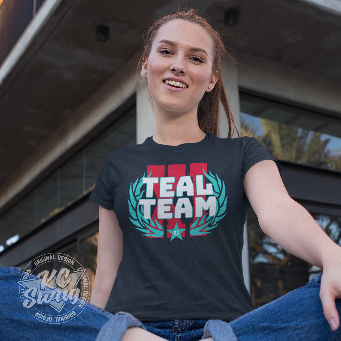 KC Swag - Kansas City Current, Teal Team XI design on navy unisex t-shirt worn by female model sitting on ground outside of apartment building