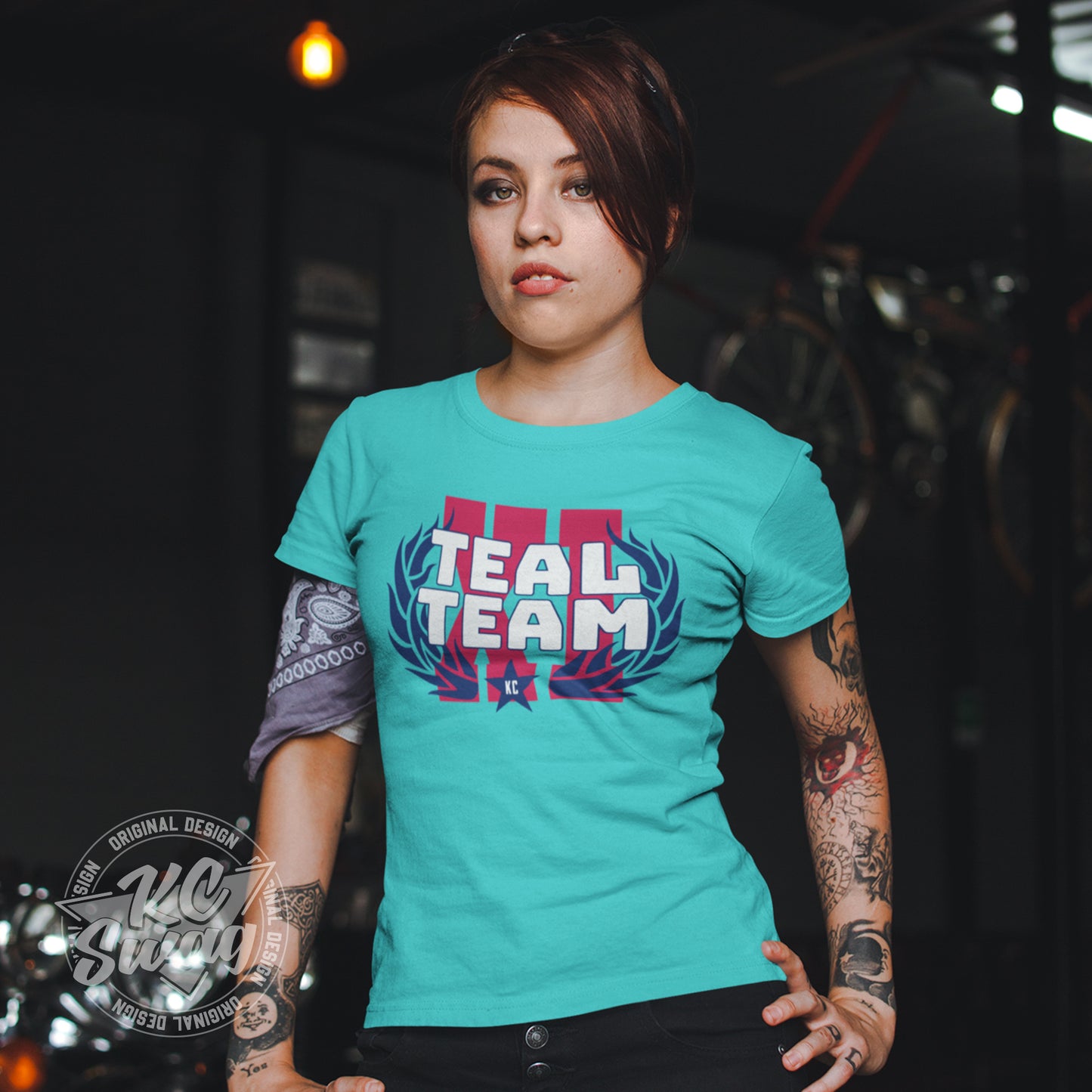 KC Swag - Kansas City Current, Teal Team XI design on teal unisex t-shirt worn by female model standing in a dark garage next to a motorcycle