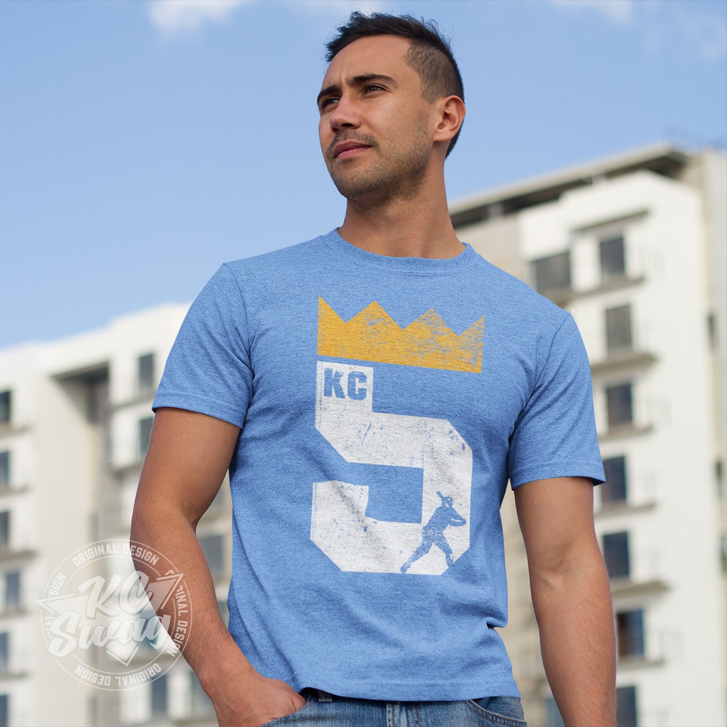 KC Swag - Kansas City Royals, Brett Five Crown design on heather columbia blue unisex t-shirt worn by male model standing in front of a large apartment complex