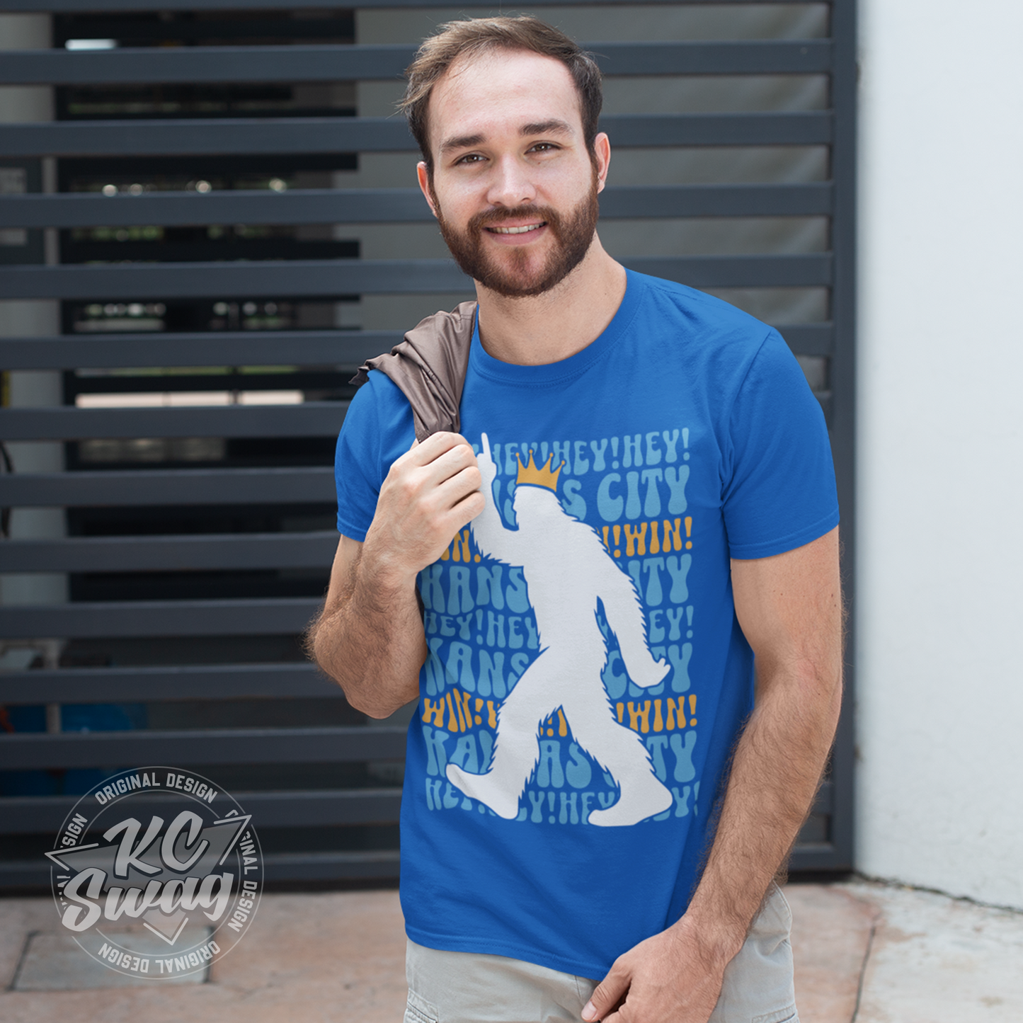 KC Swag - Kansas City Royals HEY HEY HEY PASQUATCH on a true royal blue unisex t-shirt worn by male model with jacket over his shoulder in front of a large metal gate