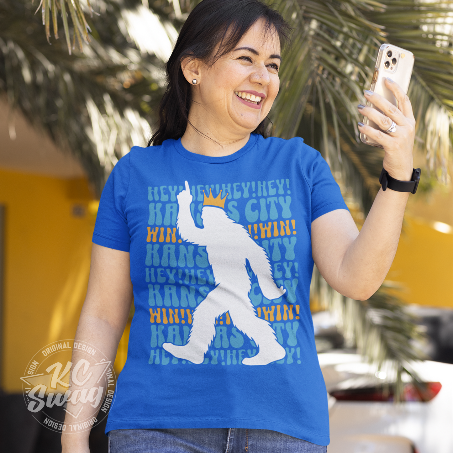 KC Swag - Kansas City Royals HEY HEY HEY PASQUATCH on a true royal blue unisex t-shirt worn by female model smiling at her phone while walking in an open-air plaza