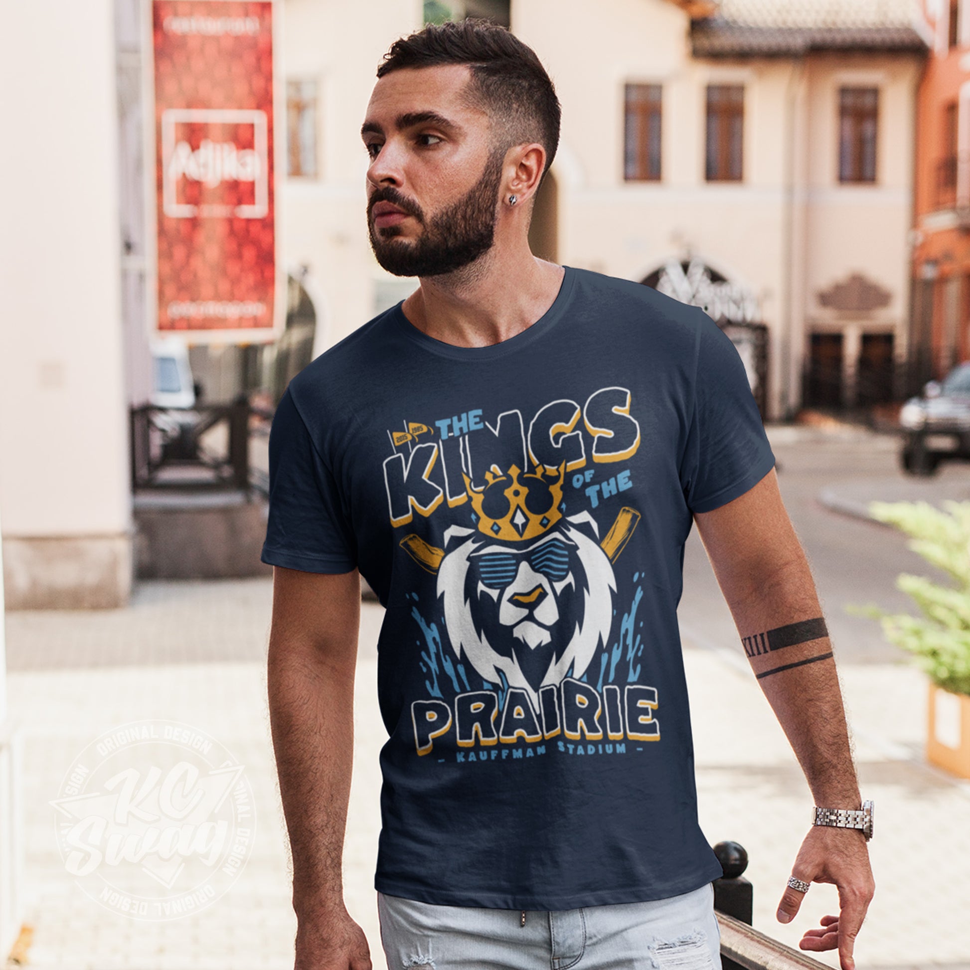 KC Swag - Kansas City Royals, Kings Of The Prairie design on navy blue unisex t-shirt worn by male model walking through an open-air plaza