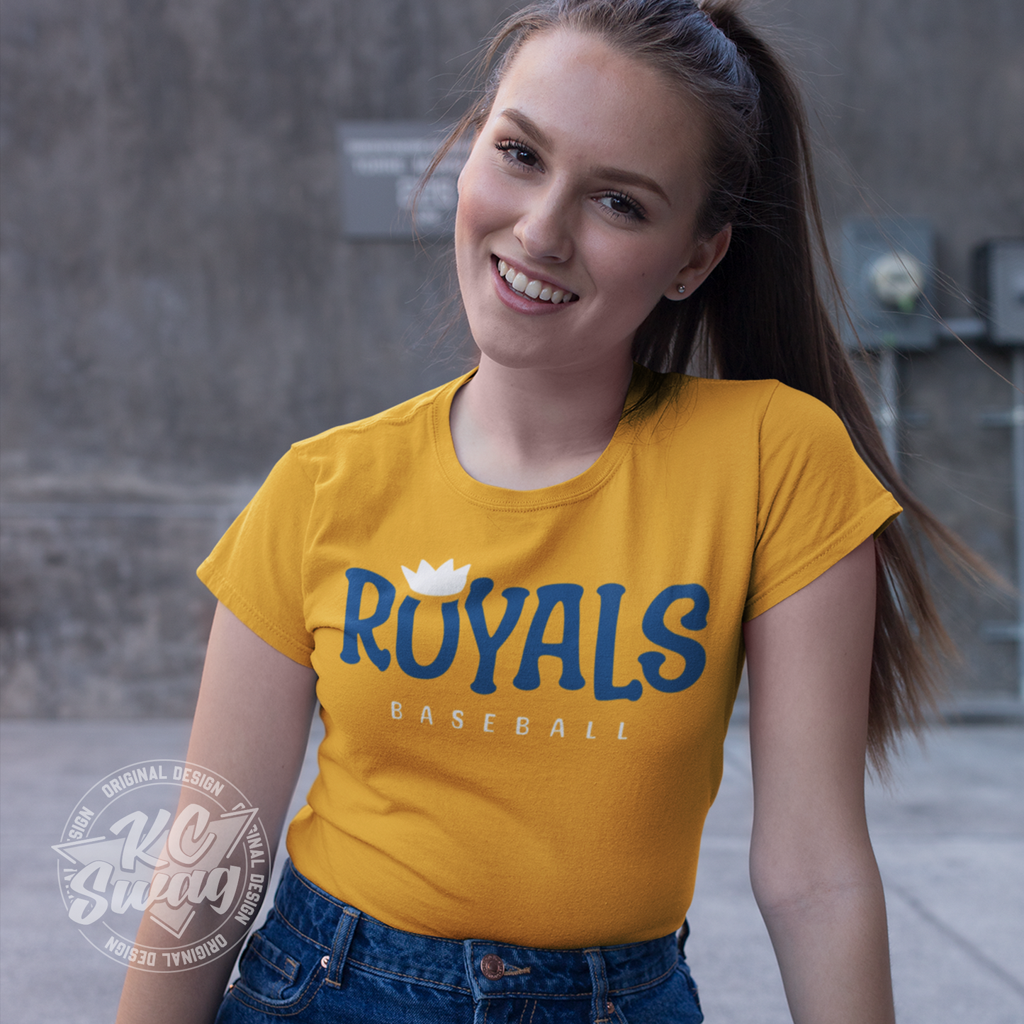 KC Swag - Kansas City Royals, Royals O-Crown design on gold unisex t-shirt worn by female model sitting in front of a concrete wall in an urban alley