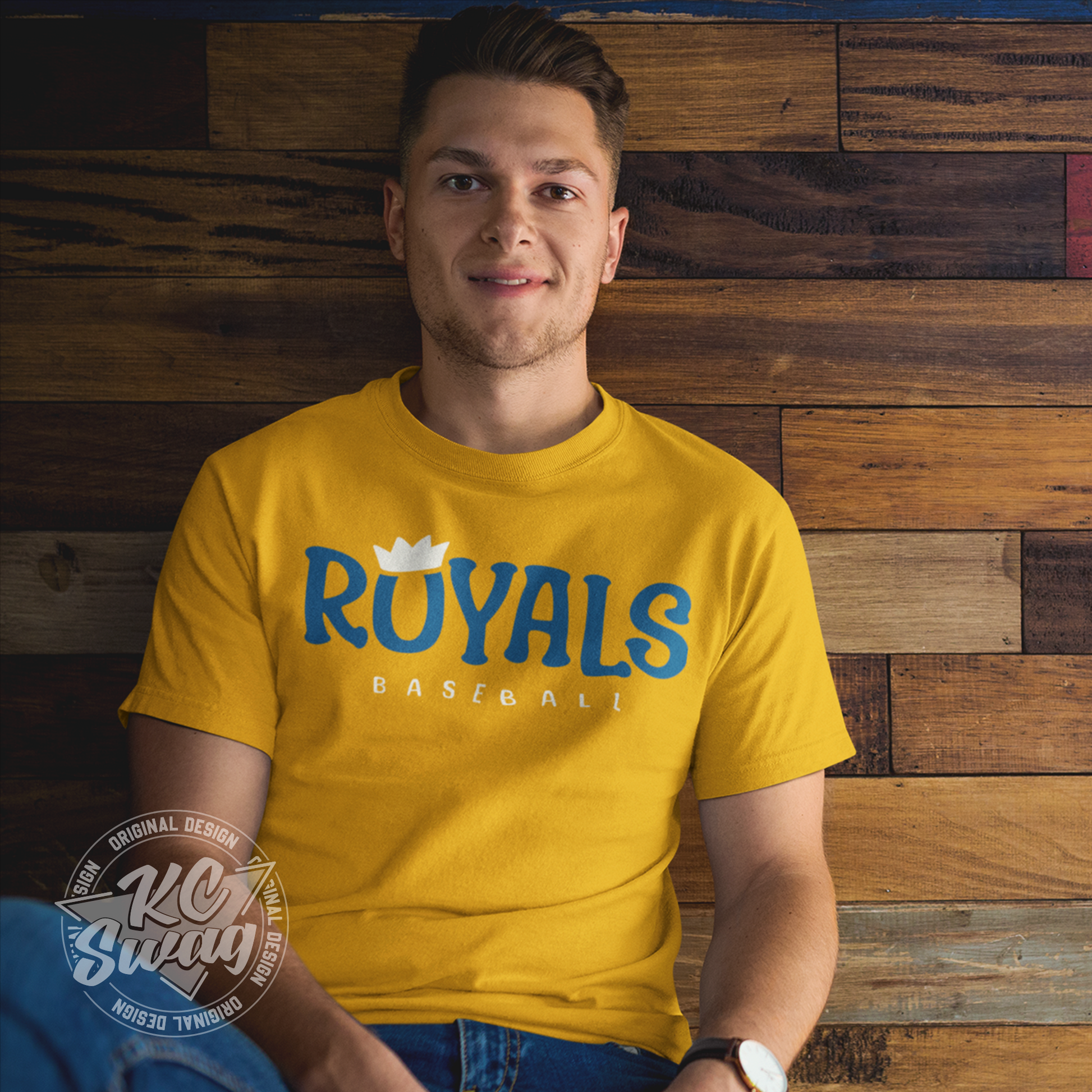KC Swag - Kansas City Royals, Royals O-Crown design on gold unisex t-shirt worn by male model sitting on floor in front of a wood wall