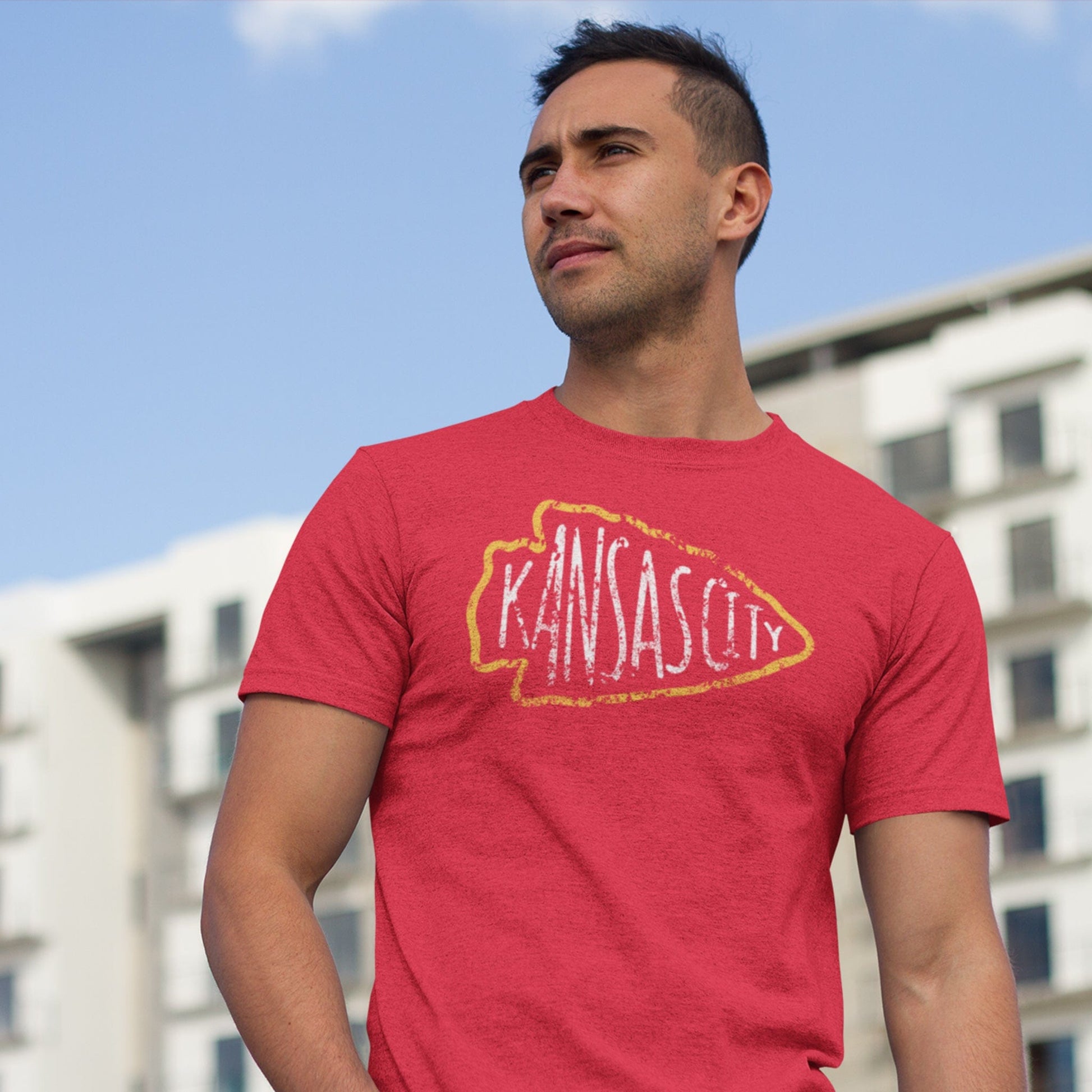 KC Swag | Kansas City Chiefs white KANSA CITY inside yellow arrowhead outline on heather red t-shirt worn by male model in front of apartment building