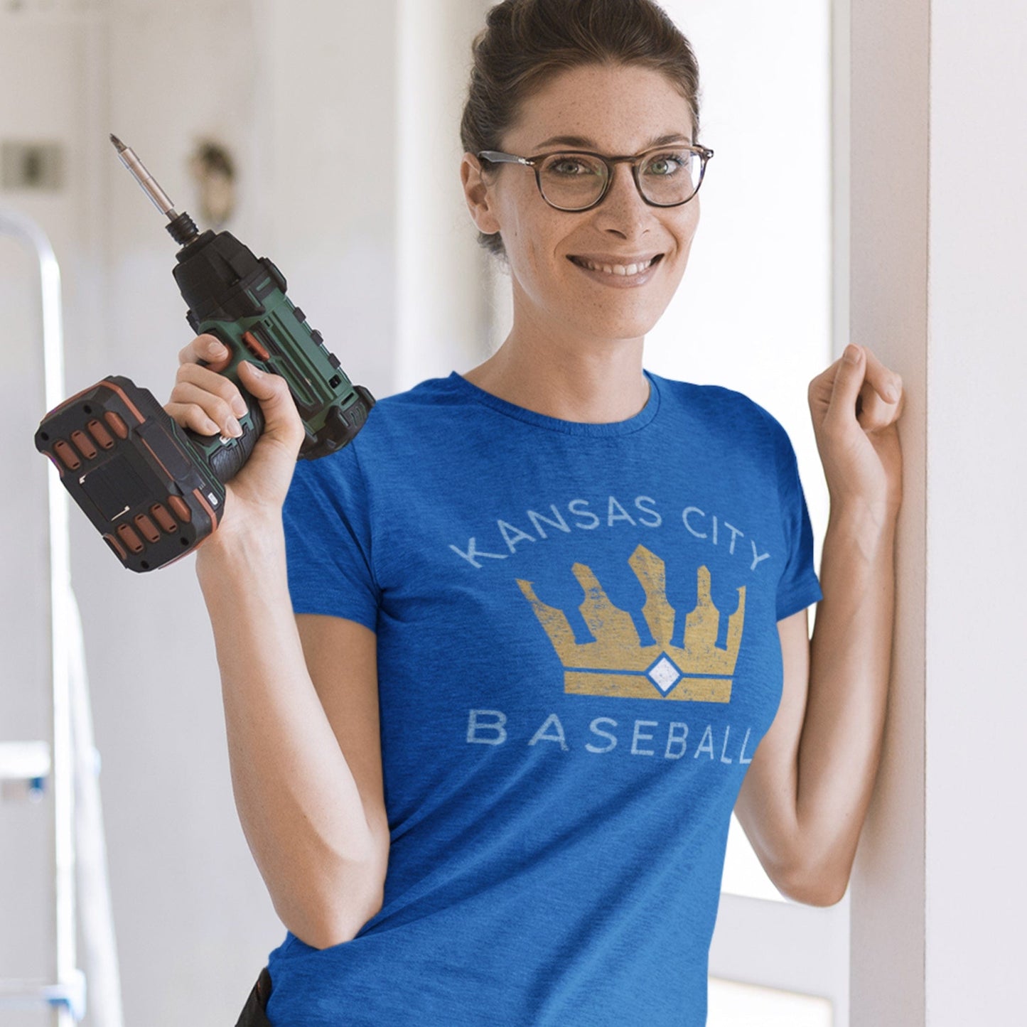 KC Swag Kansas City Royals light blue/gold KANSAS CITY BASEBALL BOTTLE CROWN on heather royal t-shirt worn by female model holding drill inside home