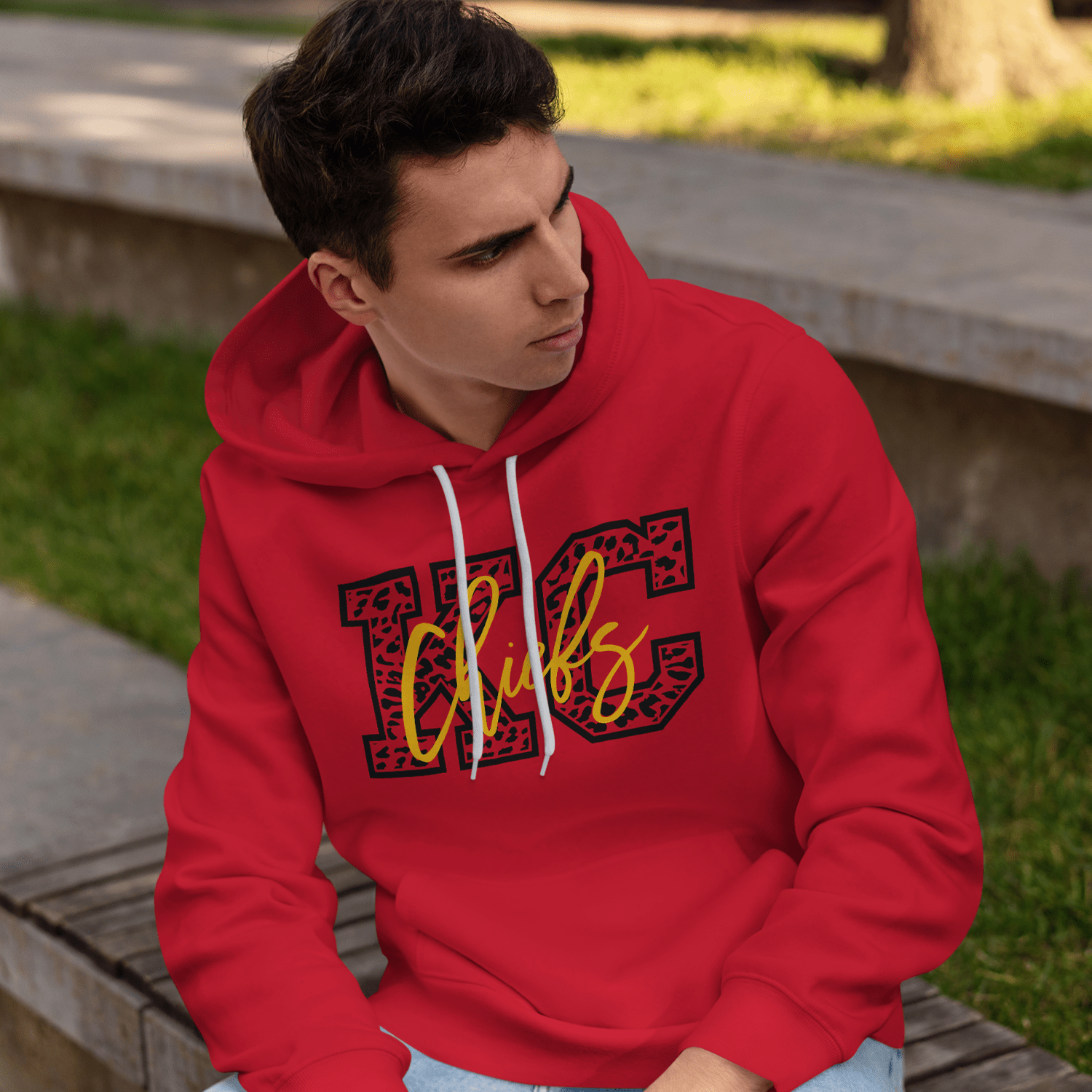 KC Swag Kansas City Chiefs yellow CHIEFS on black cheetah pattern KC on red fleece pullover hoodie worn by male model sitting on bench in public park
