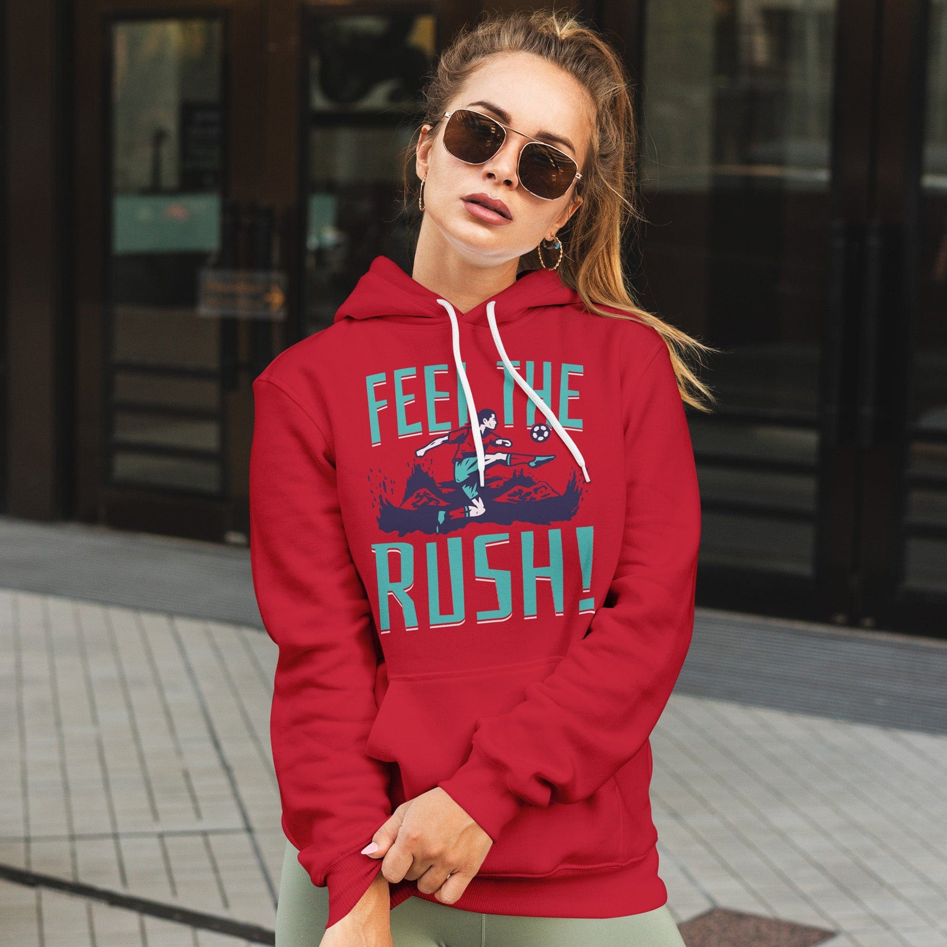 KC Swag Kansas City Current FEEL THE RUSH on red fleece pullover hoodie worn by female model standing outside of department store doors