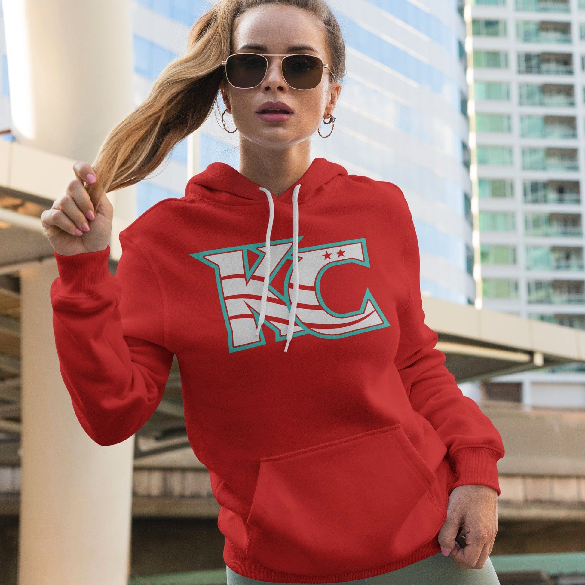 KC Swag Kansas City Current CURRENT KC on red fleece pullover hoodie worn by female model standing in front of downtown buildings
