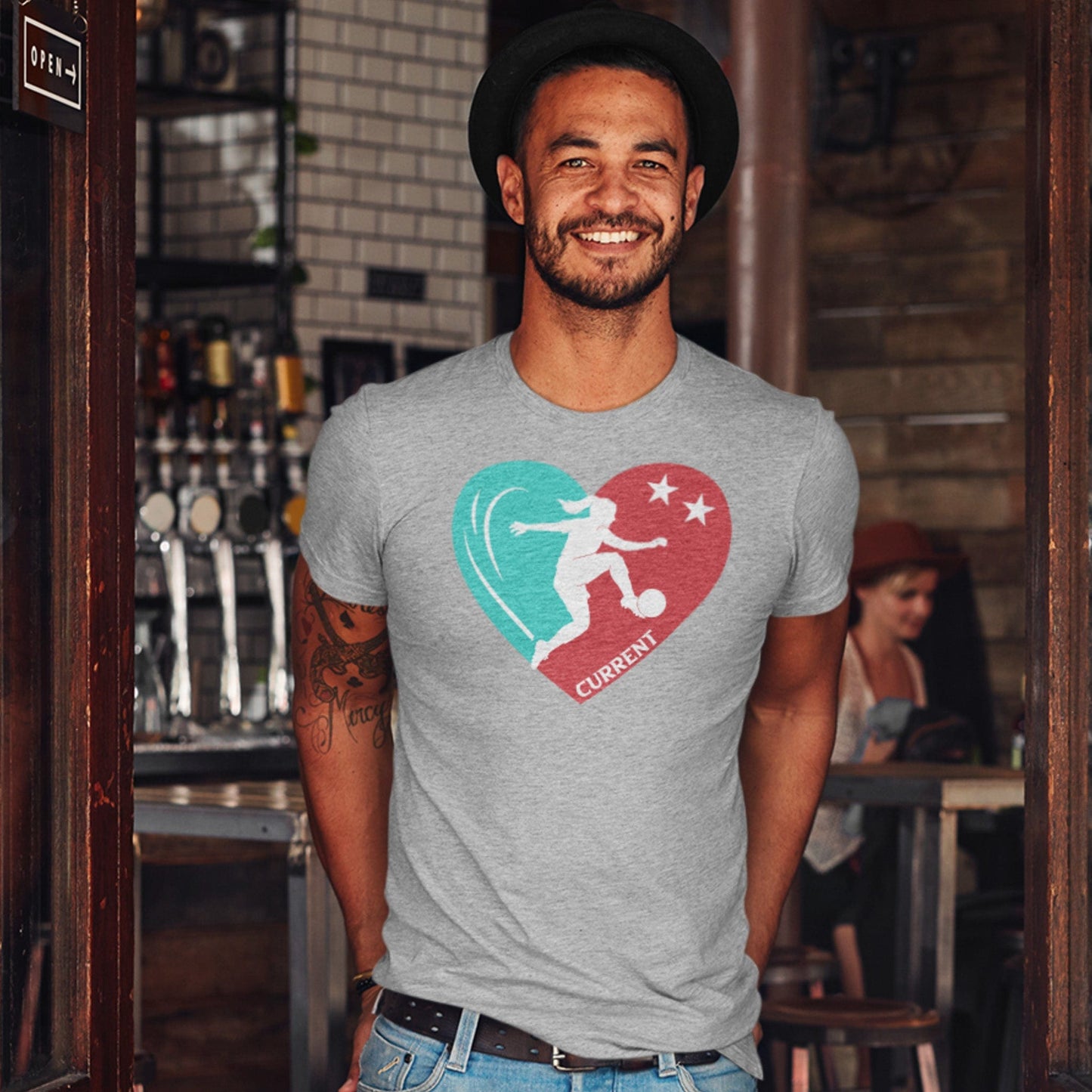 KC Swag Kansas City Current PLAYER HEART on an athletic heather grey unisex t-shirt worn by male model standing in pub doorway