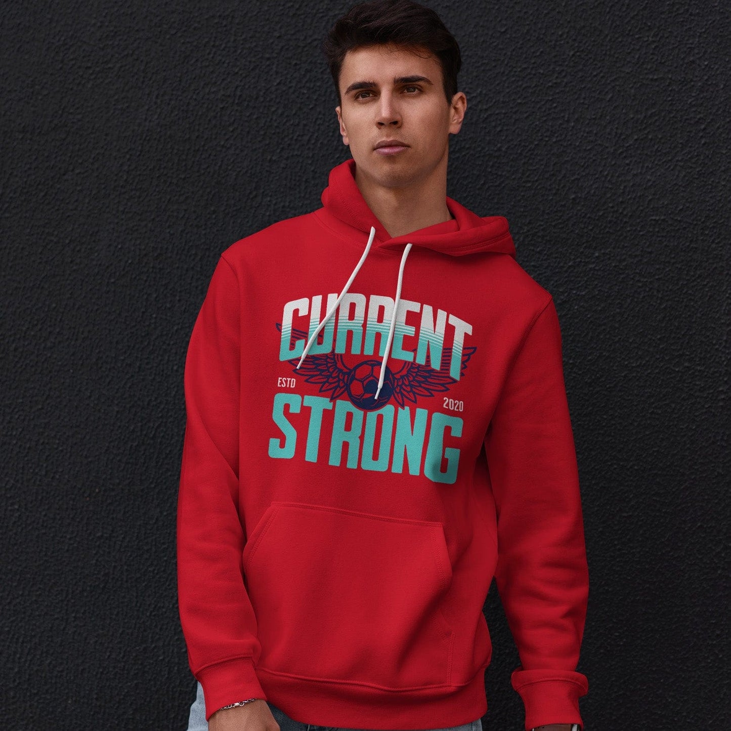 KC Swag Kansas City Current CURRENT STRONG on red fleece pullover hoodie worn by male model leaning against a dark grey concrete wall