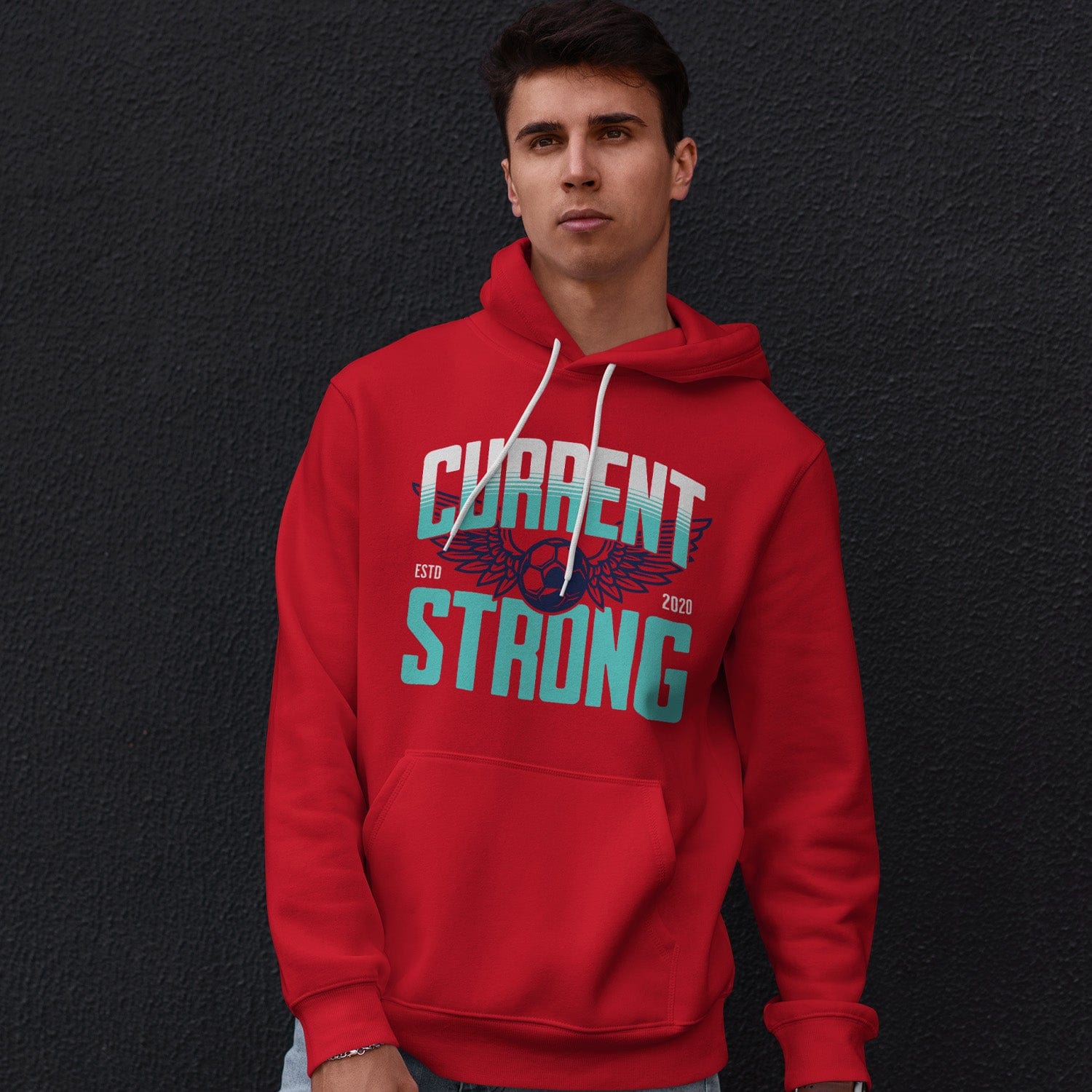 KC Swag Kansas City Current CURRENT STRONG on red fleece pullover hoodie worn by male model leaning against a dark grey concrete wall
