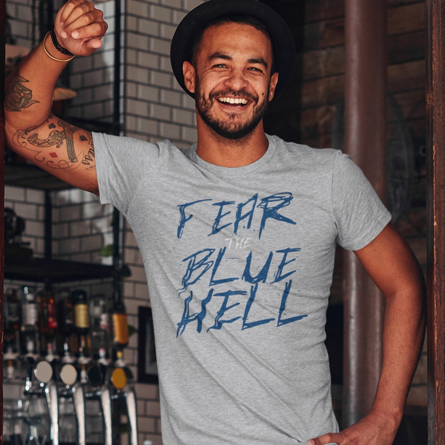 KC Swag Sporting Kansas City navy blue/white FEAR THE BLUE HELL on athletic heather grey t-shirt worn by male model standing in pub doorway