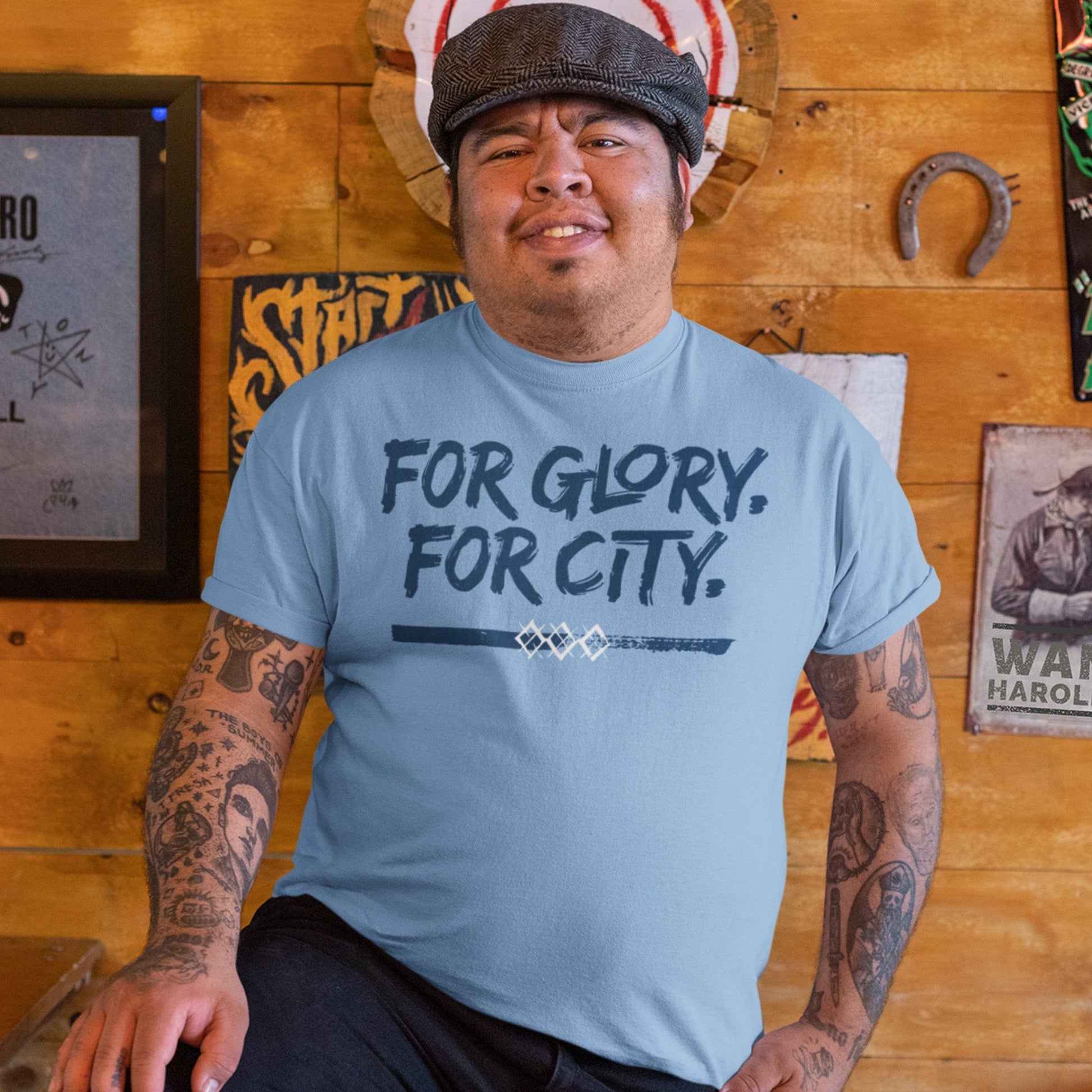 KC Swag Sporting Kansas City navy, powder, white FOR GLORY FOR CITY on baby blue unisex t-shirt  worn by male model standing against wood wall inside bar