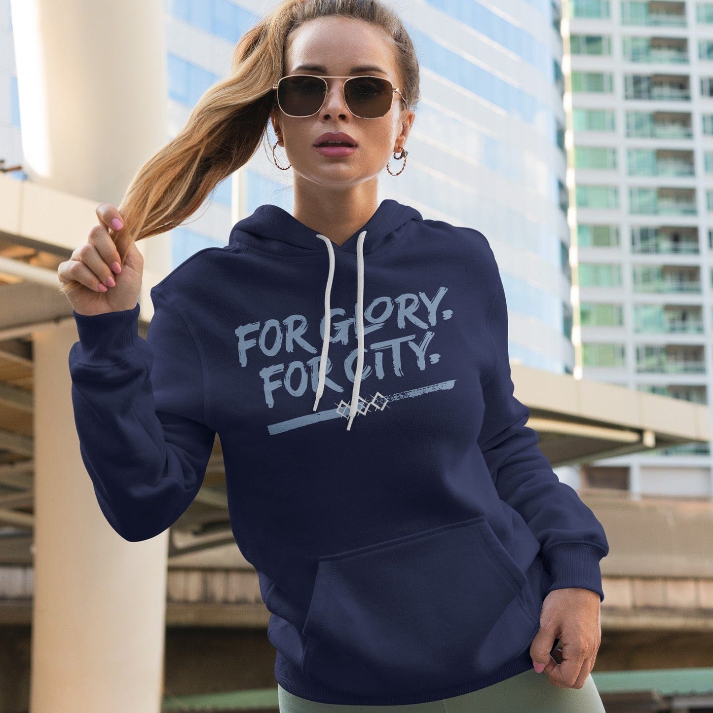 KC Swag Sporting Kansas City navy, powder, white FOR GLORY FOR CITY on navy pullover fleece hoodie worn by female model standing in front of downtown buildings