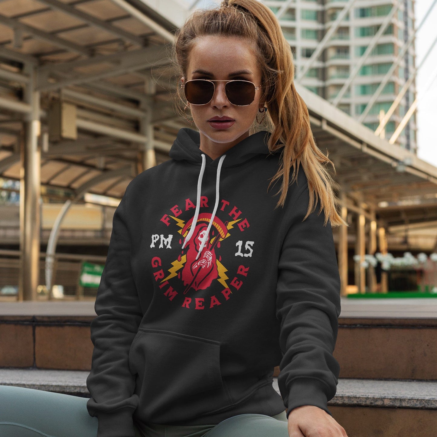 KC Swag Kansas City Chiefs GRIM REAPER PM15 on black fleece pull-over hoodie worn by female model sitting on steps in front of downtown structure