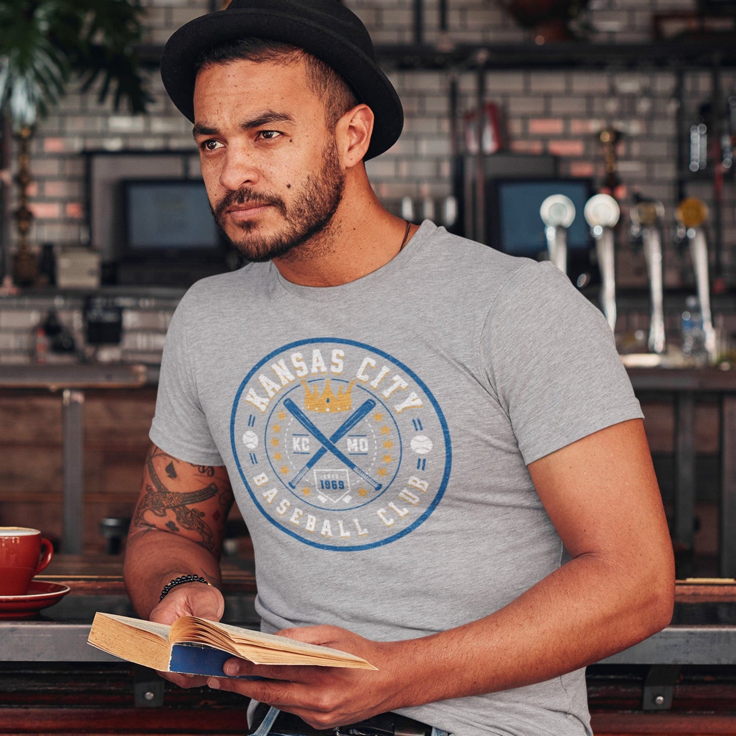 KC Swag Kansas City Royals blue, gold, white KC BASEBALL CLUB on athletic heather grey unisex t-shirt worn by male model seated at bar in pub