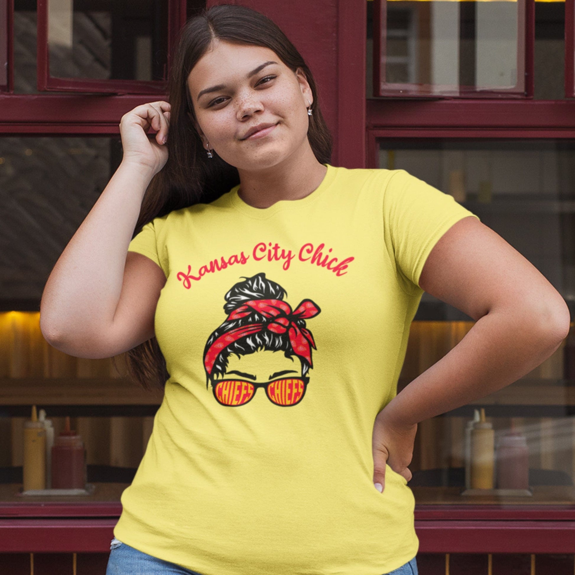 KC Swag Kansas City Chiefs red/black/yellow KANSAS CITY CHICK with girl in bandana and CHIEFS sunglasses graphic on yellow t-shirt worn by female model in front of restaurant windows