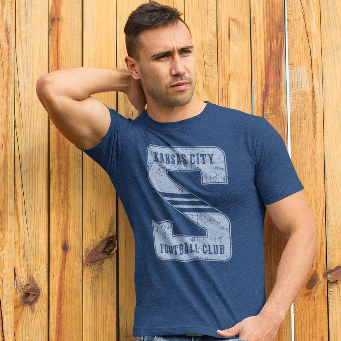 KC Swag Sporting Kansas City light blue KANSAS CITY FOOTBALL CLUB on giant striped S on heather navy t-shirt worn by male model leaning on wood fence