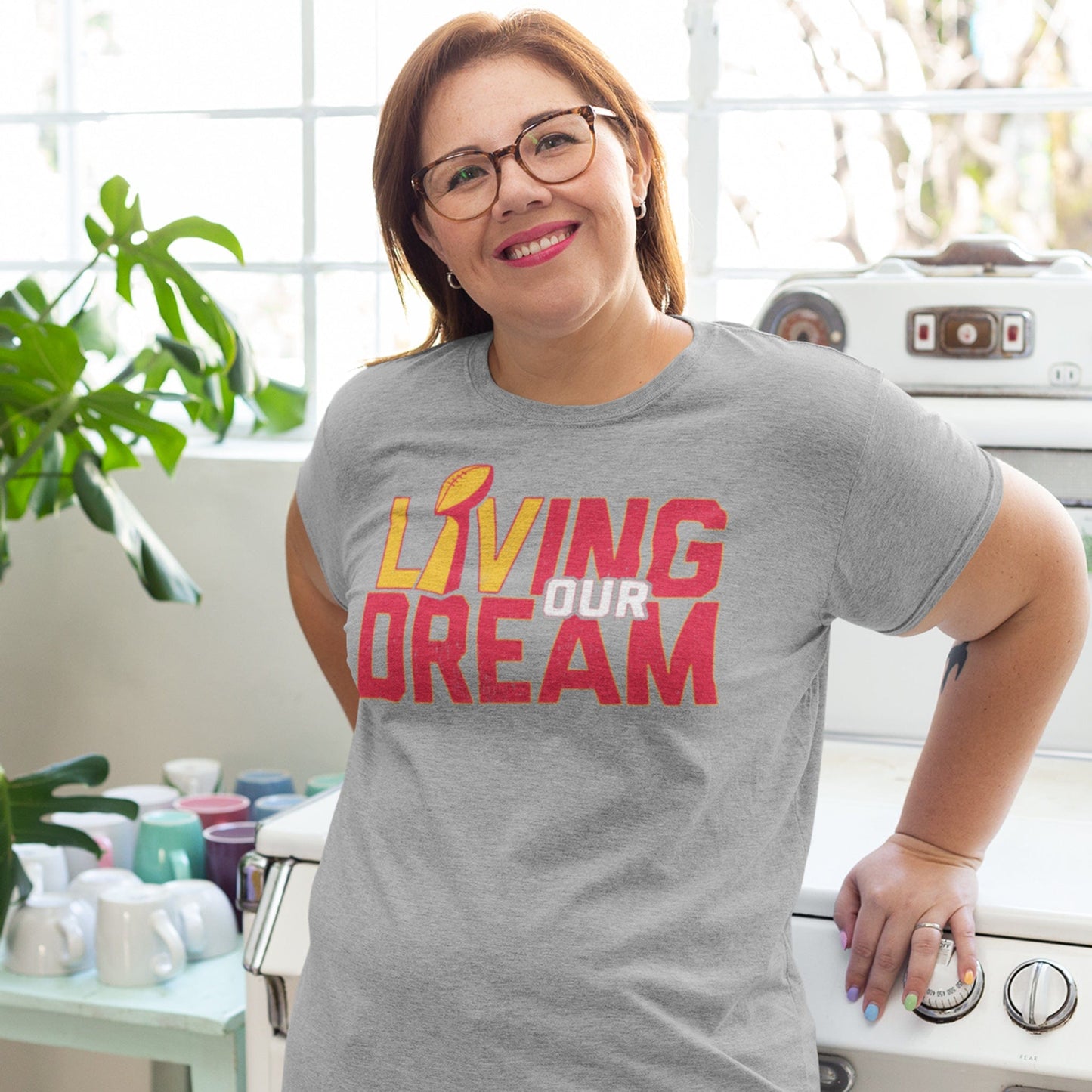 KC Swag Kansas City Chiefs red/yellow/white L(Lombardi trophy)IVING OUR DREAM on athletic heather grey t-shirt worn by female model in bright kitchen