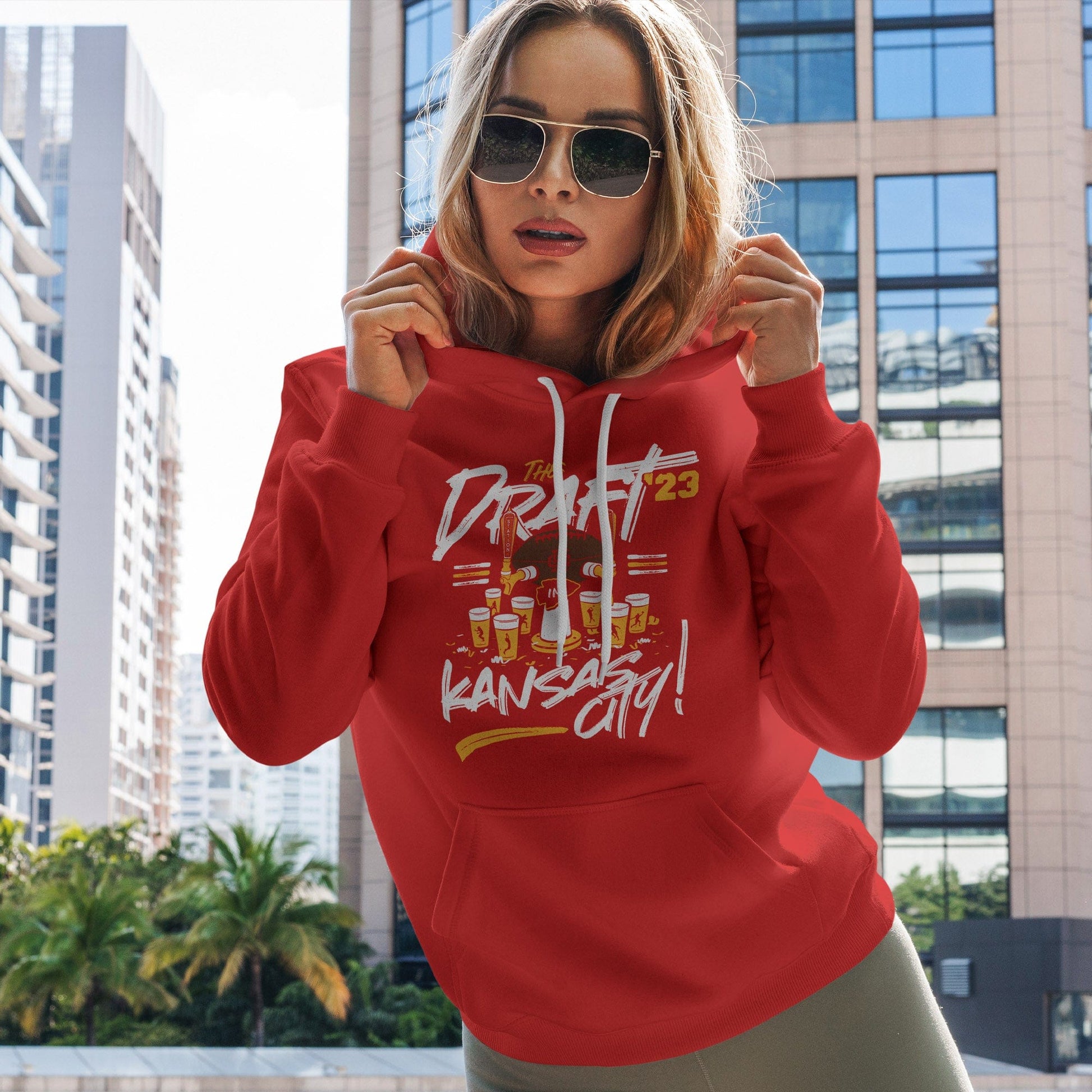 KC Swag Kanssas City Chiefs DRAFTIN' IN KC on red pullover fleece hoodie worn by female model standing on downtown balcony