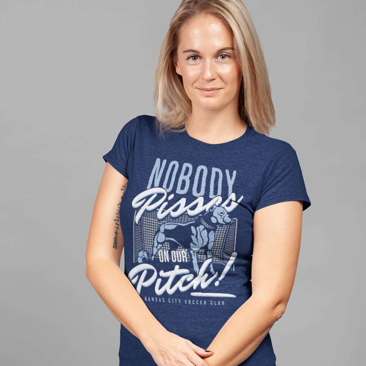 KC Swag Sporting Kansas City navy, powder, white, grey PITCH PROTECTOR on heather navy unisex t-shirt worn by female model standing in front of a gray studio wall