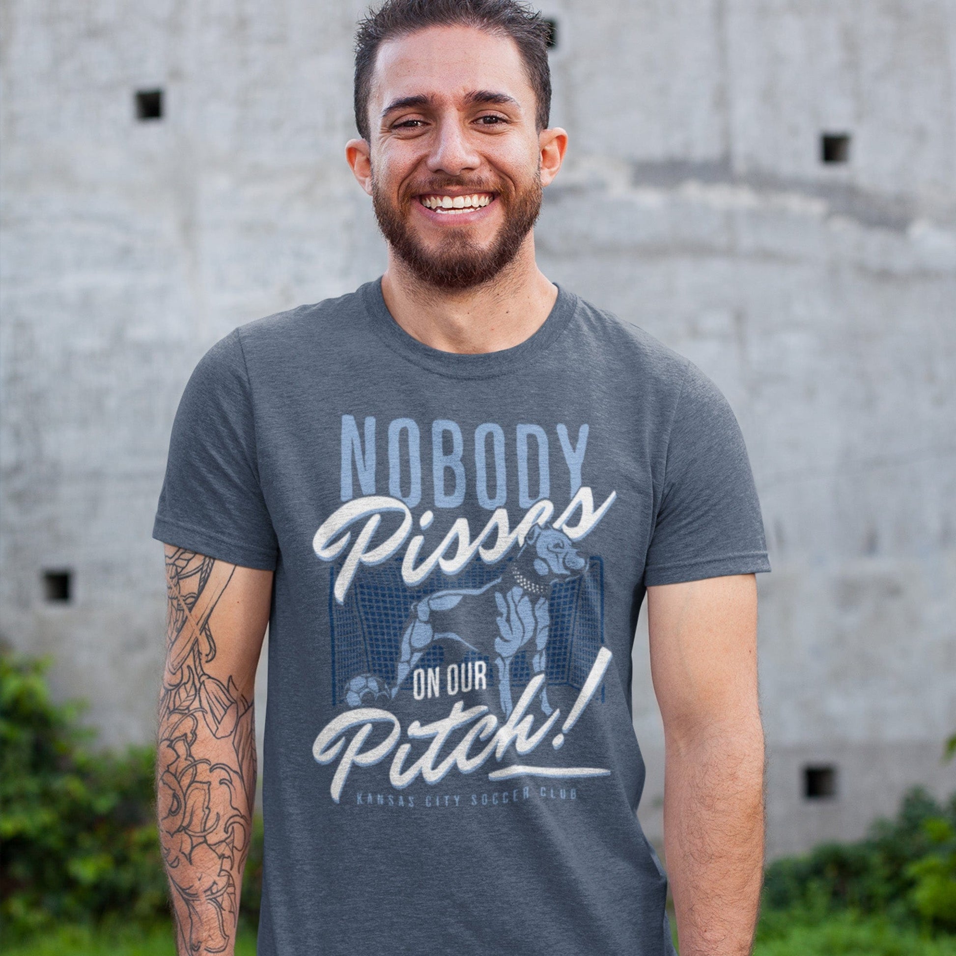 KC Swag Sporting Kansas City navy, powder, white, grey PITCH PROTECTOR on heather slate unisex t-shirt worn by male model standing in yard in front of concrete wall