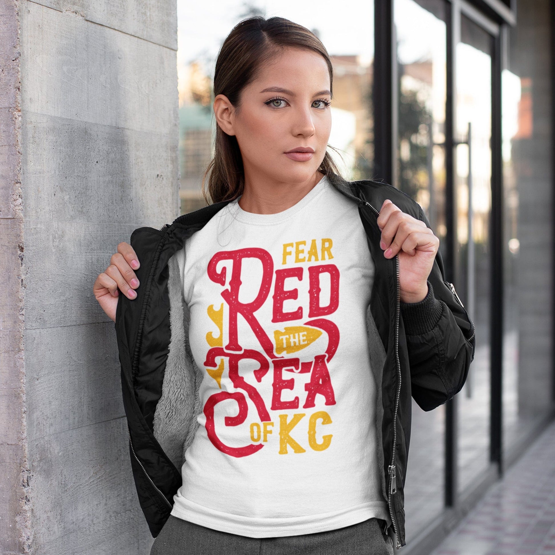 KC Swag Kansas City Chiefs SEA OF RED on white t-shirt worn by female model under a black jacket on an urban sidewalk