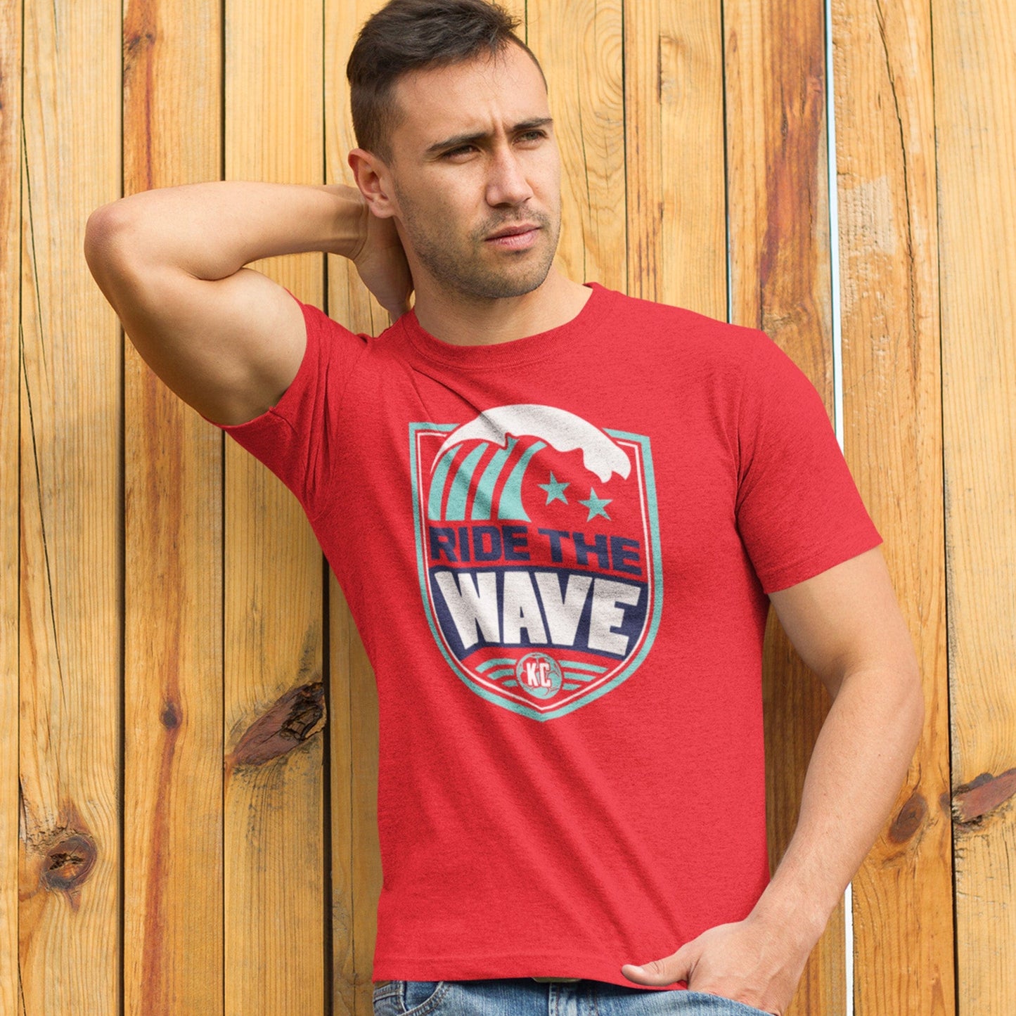 KC Swag Kansas City Current RIDE THE WAVE on heather red unisex t-shirt worn by male model standing in front of yellow wooden fence