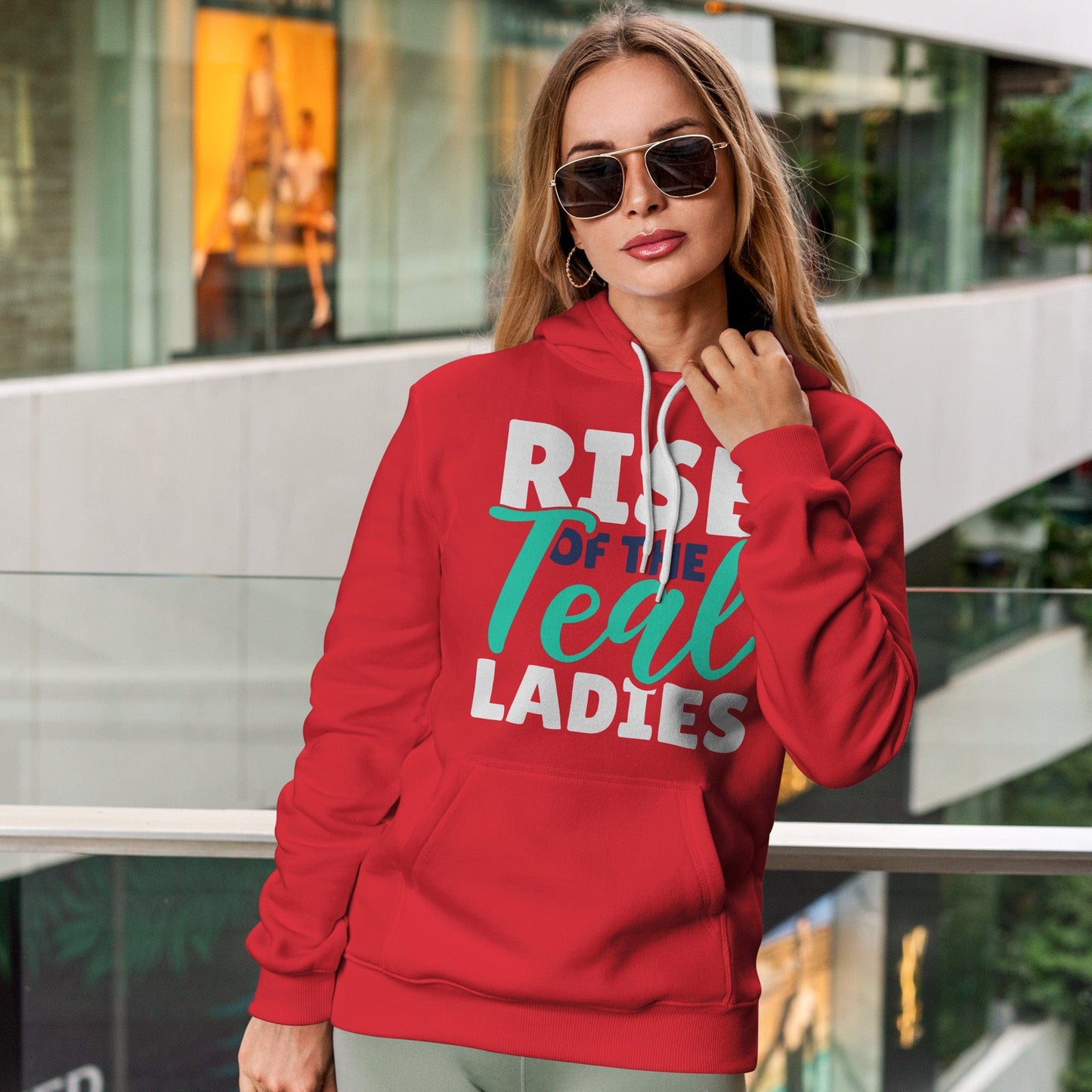 KC Swag Kansas City Current TEAL LADIES RISE on red fleece pullover hoodie worn by female model leaning on rail in shopping mall