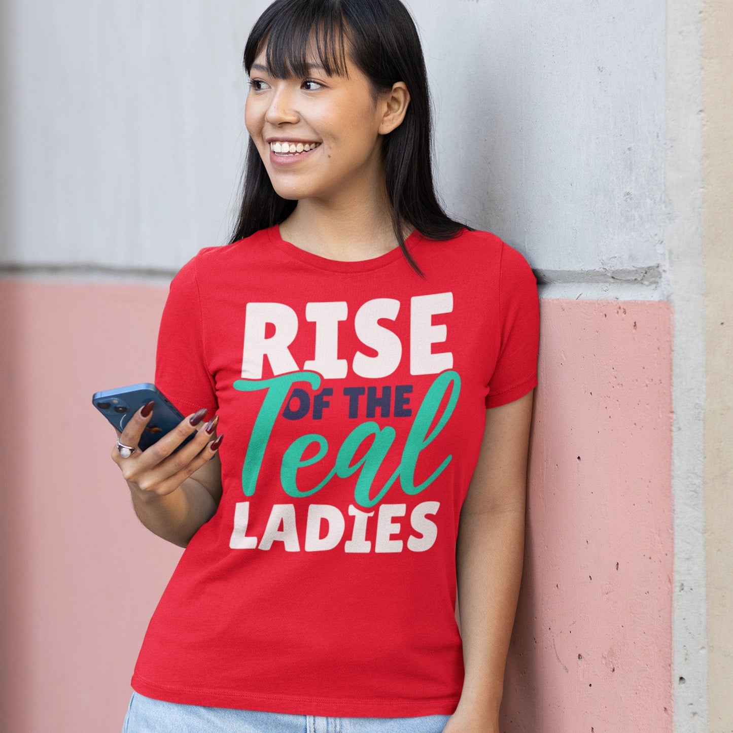 KC Swag Kansas City Current RISE OF THE TEAL LADIES on red unisex t-shirt worn by female model leaning on pink concrete wall while holding phone
