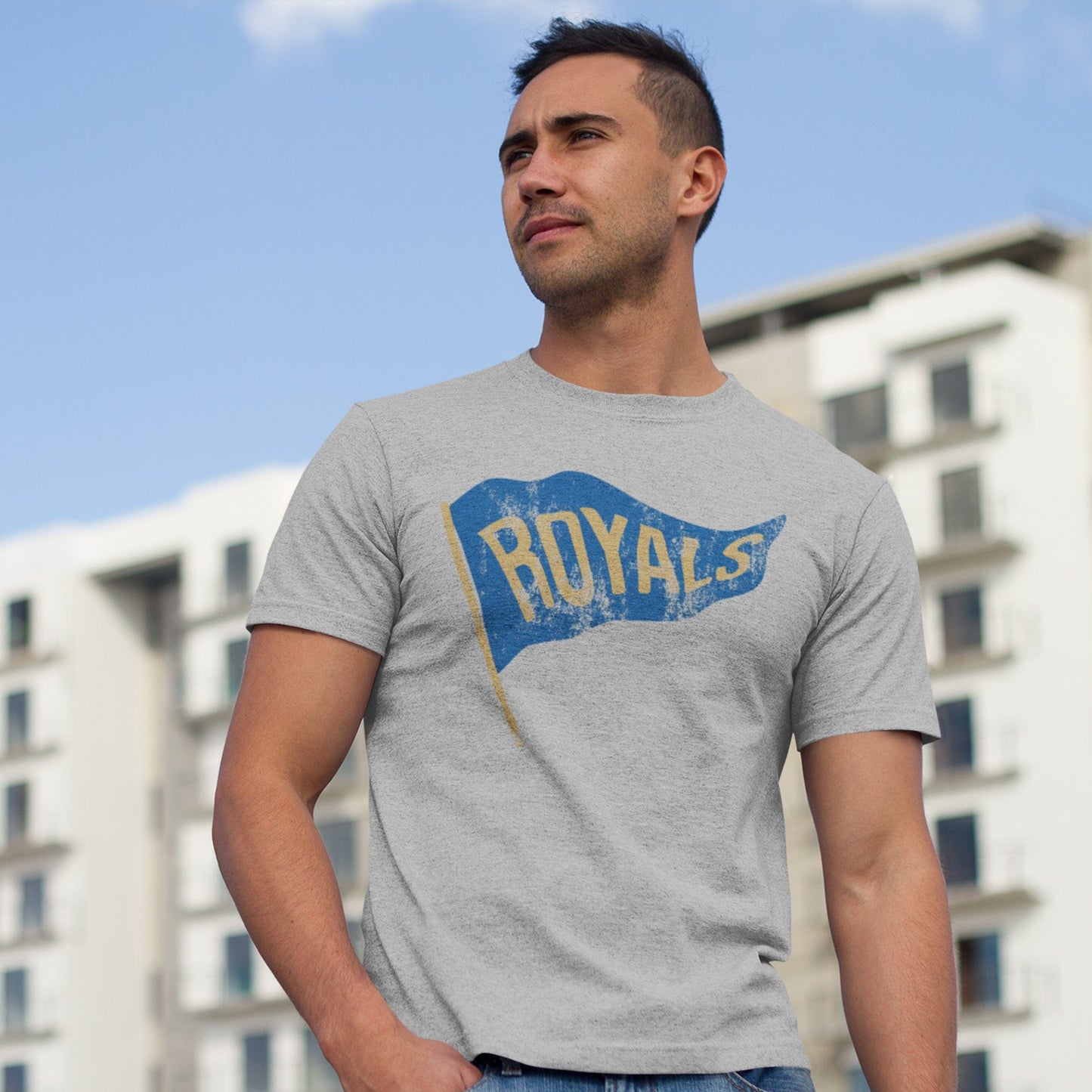 KC Swag Kansas City Royals blue/gold ROYALS PENNANT on athletic heather grey t-shirt worn by male model in front of apartment building