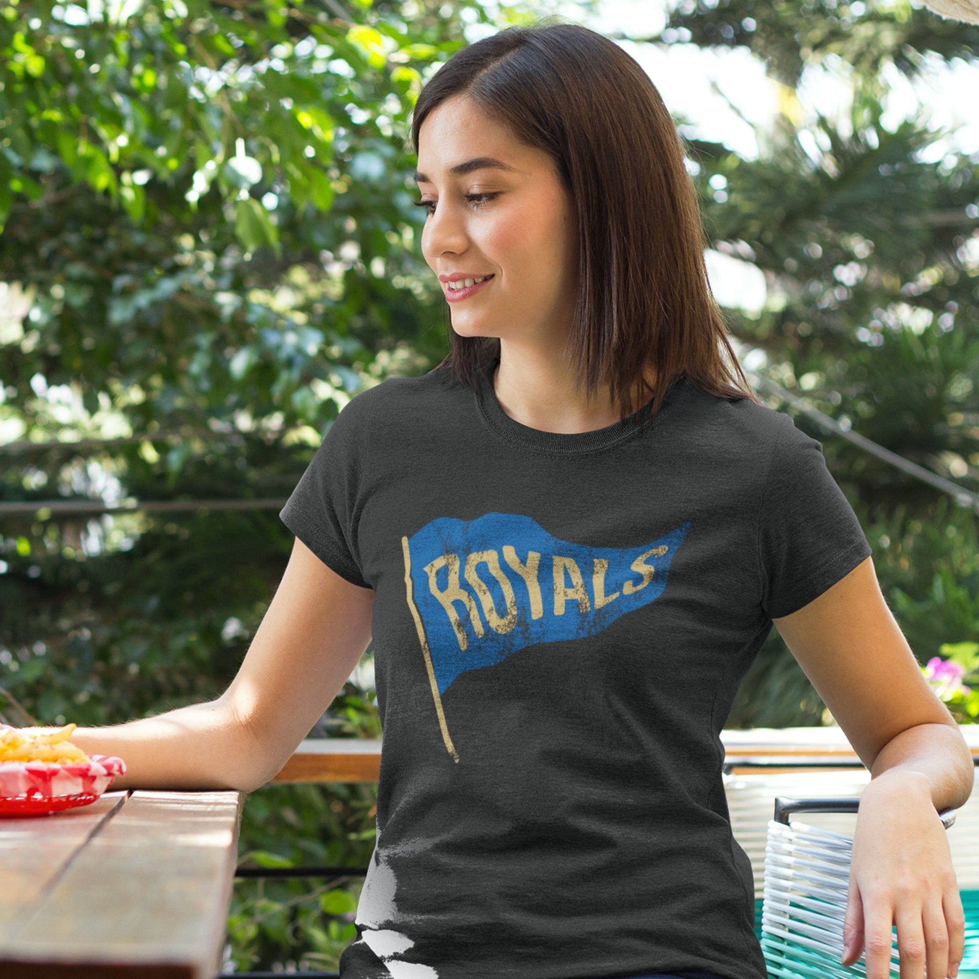 KC Swag Kansas City Royals blue/gold ROYALS PENNANT on dark heather grey t-shirt worn by female model seated at picnic table on outdoor patio