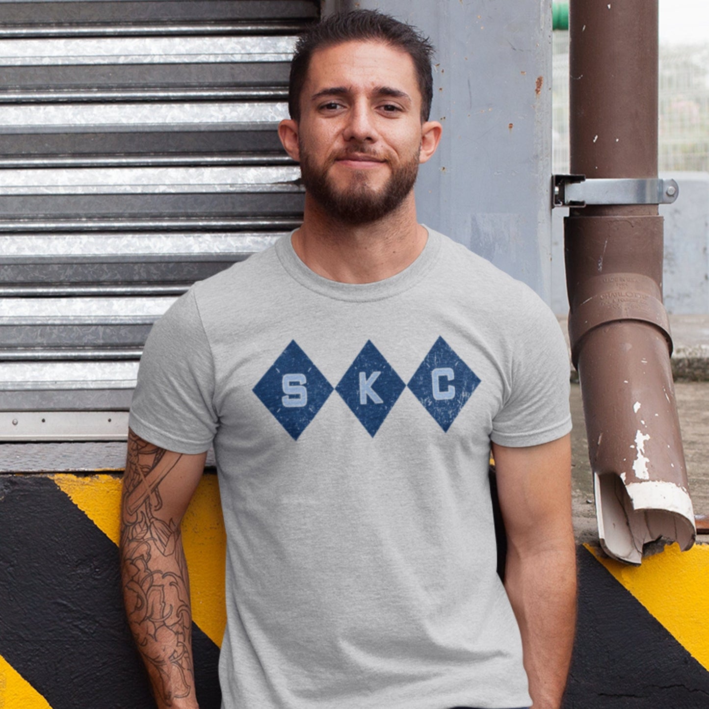 KC Swag Sporting Kansas City powder blue/navy SKC DIAMONDS with argyle stitching on athletic heather grey t-shirt worn by male model leaning against urban loading dock